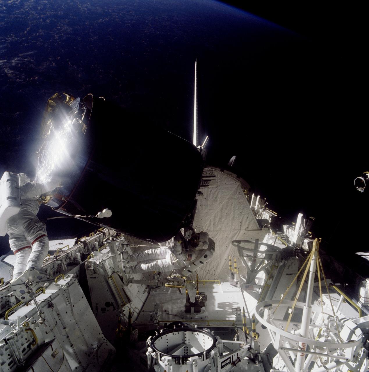 51A-41-058 (12 November 1984) --- Astronaut Joseph P. Allen IV appears to be lifting weights. Astronaut Dale A. Gardner holding on. Actually, Dr. Allen is the sole anchor for the top portion (and most of) the captured Palapa B-2 communications satellite during the Nov. 12 retrieval extravehicular activity (EVA) of the two mission specialists. This scene came near the end of the long-duration task. Gardner used a torque wrench to tighten clamps on an adapter used to secure the Palapa to its "parking place" in Discovery's cargo bay. Note the difference between the two stinger devices stowed on Challenger's port side (right side of frame). The one nearer the spacecraft's vertical stabilizer is spent, having been inserted by Allen earlier in the day to stabilize the communications satellite. The one nearer the camera awaited duty in two days when it would aid in the capture of the Westar VI satellite. 