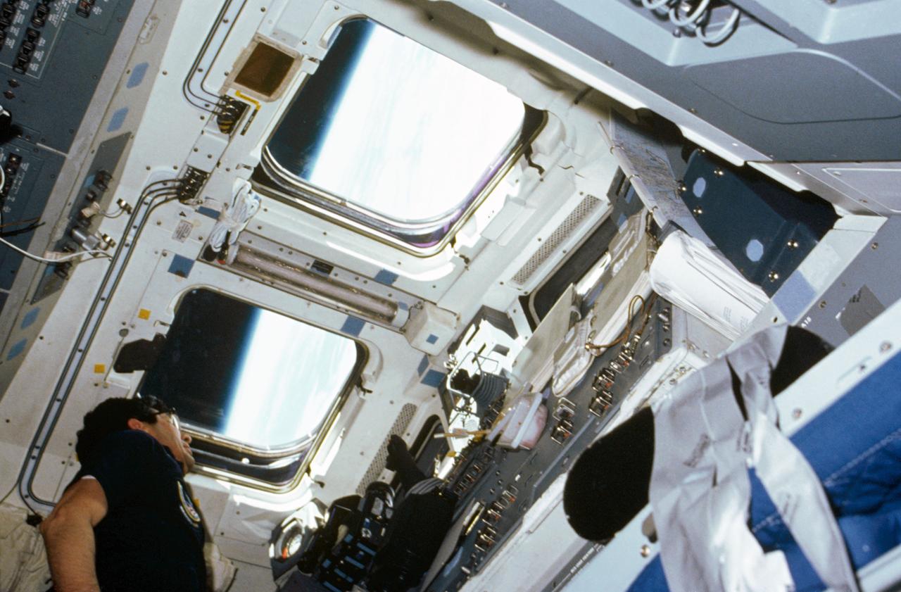 In this low-angle photo Payload specialist Lodewijk van den Berg, one of two payload specialists, looks out aft flight deck window aboard the shuttle orbiter Challenger.