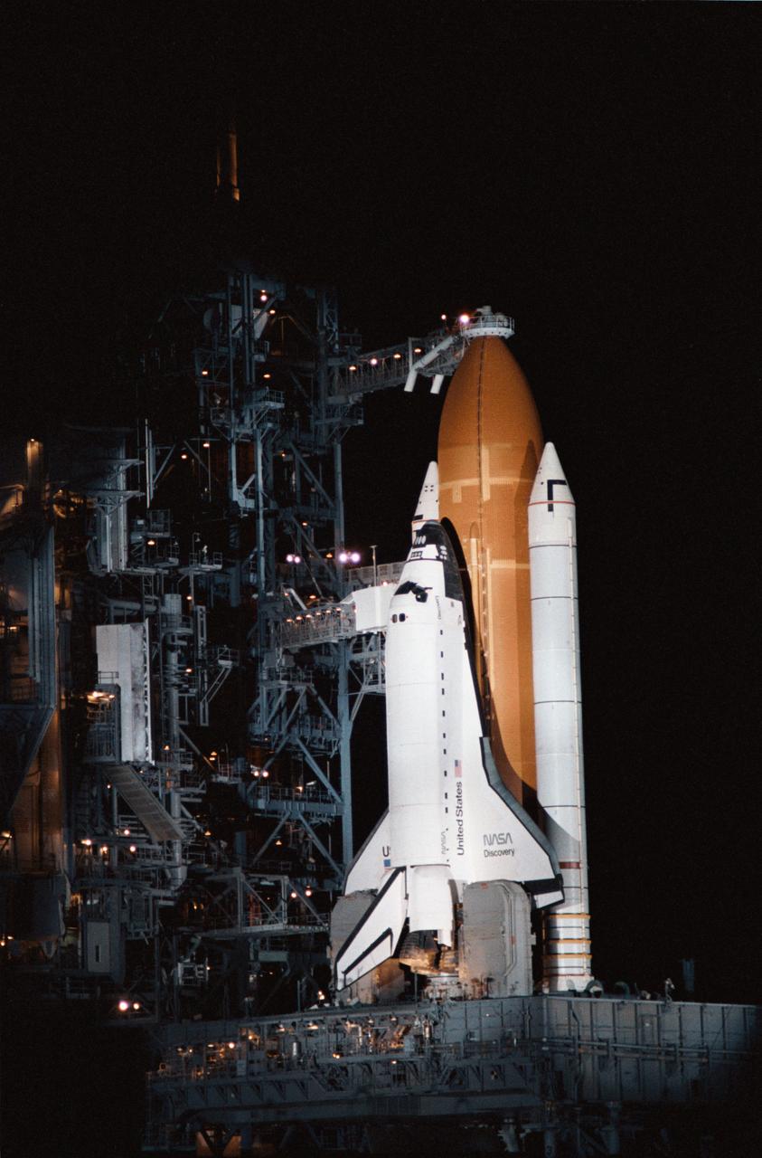 View of the shuttle Discovery on the launch pad just prior to STS 51-D launch. The surrounding area is dark, with the launch complex accented by spotlights.