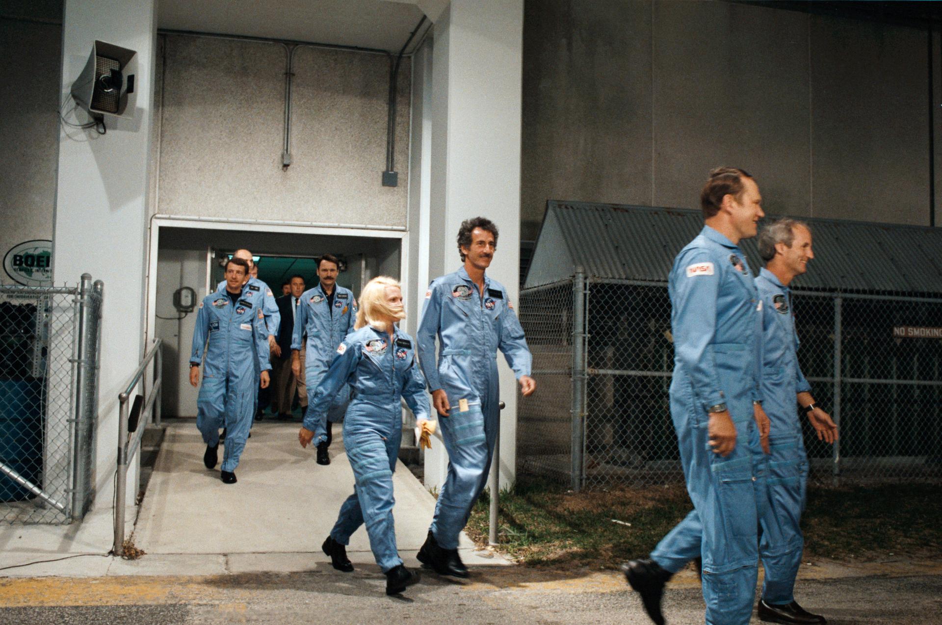 The 7 crew members of STS-51D walk out of the oeprations and checkout building at KSC prior to launch.