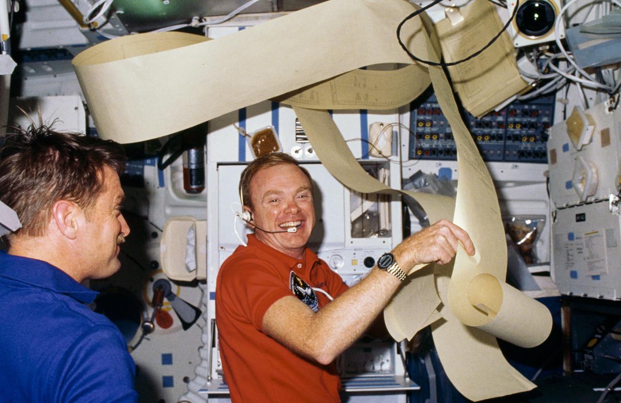 51F-03-024 (29 July-6 Aug 1985) --- Astronauts Anthony W. England, left, and Roy D. Bridges are surrounded by some of the prolific teleprinter copy transmitted from ground controllers to the Earth-orbiting Challenger. Eventually the equivalent of several football fields' length of paper was filled with data from flight  controllers.