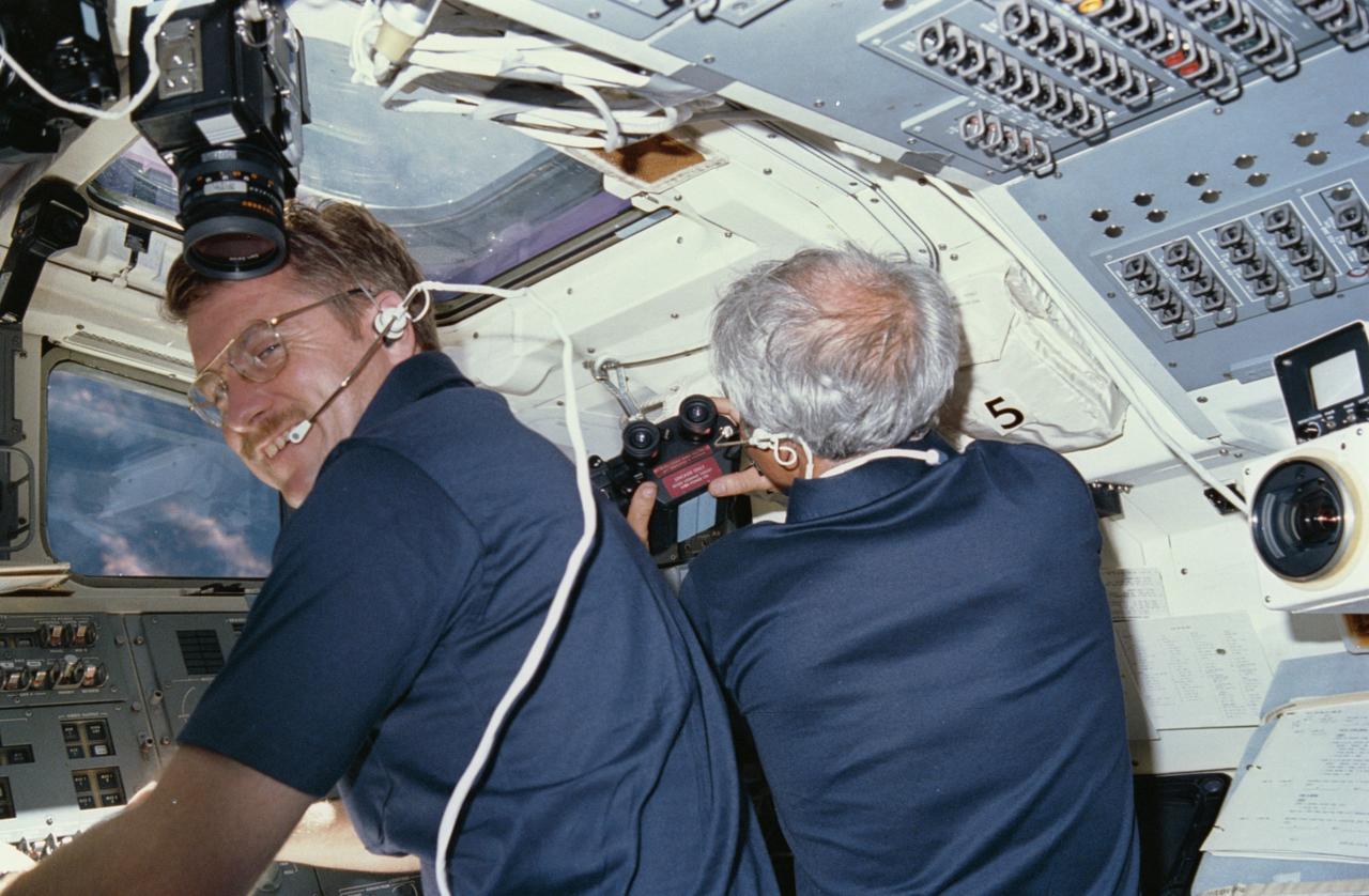 51F-05-003  (29 July-6 Aug 1985) --- Astronaut Anthony W. England, 51-F mission specialist, talks to ground controllers in Houston from the flight deck of the Earth-orbiting Challenger while Payload Specialist John-David Bartoe prepares to use binoculars through aft flight deck windows.