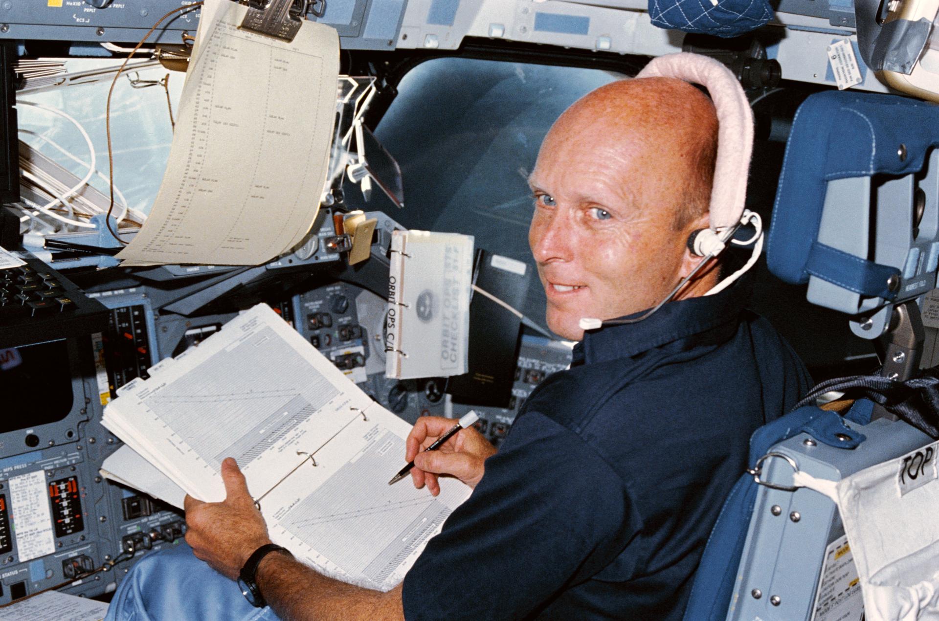 C. Gordon Fullerton wears a headset and holds a binder with charts onboard Challenger