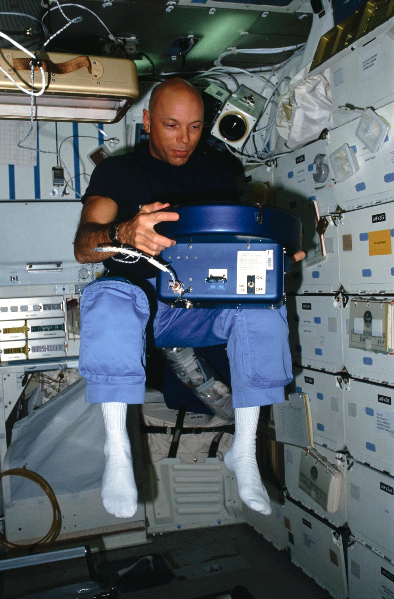 Story Musgrave floats in Challenger's middeck with a centrifuge in hand.
