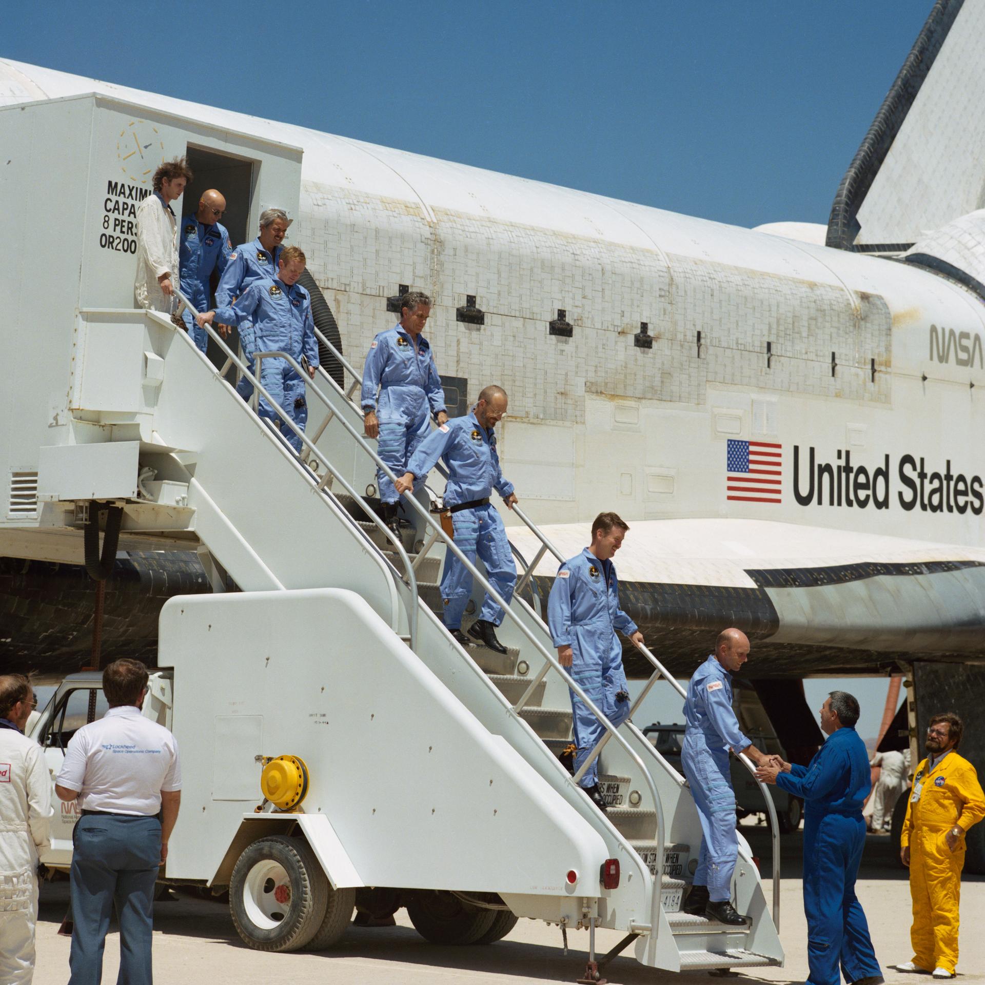 The crew of STS-51F descend a stairway from Space Shuttle Challenger at the end of their mission.