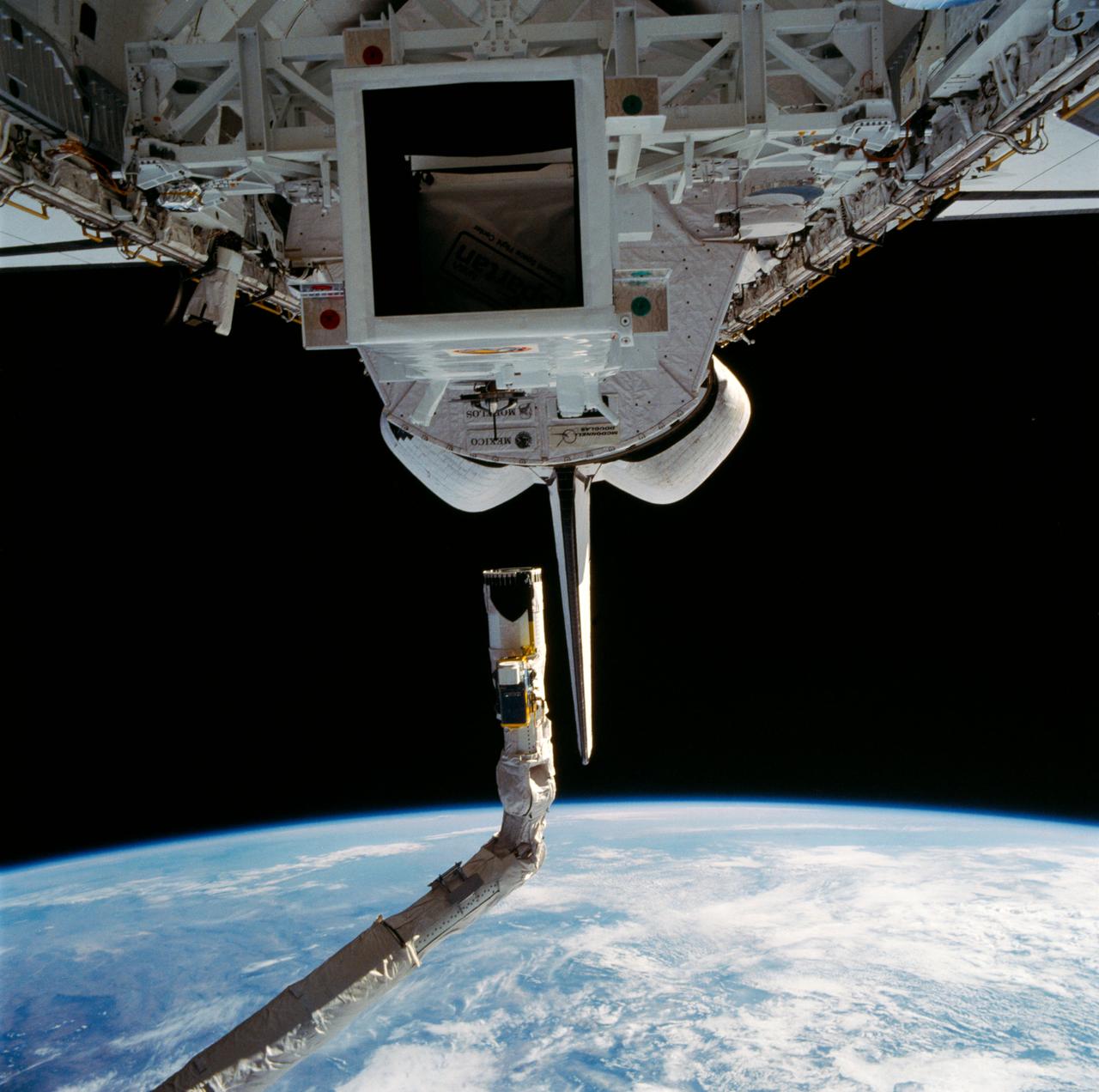 Spartan I satellte sits in the Discovery's payload bay prior to being deployed. Above it can be seen the remote manipulator system (RMS) arm and end effector. The Earth's horizon can also be seen above the orbiter.
