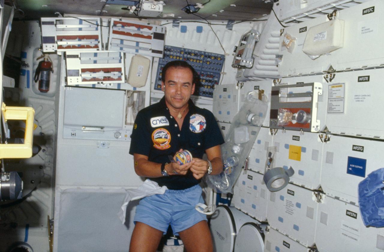 51G-08-021 (17-24 June 1985) --- Patrick Baudry, payload specialist representing the Centre National d'Etudes Spatiales of France, prepares to open a can of lobster.  The bag attached to a nearby locker door appears to contain several other French snacks.