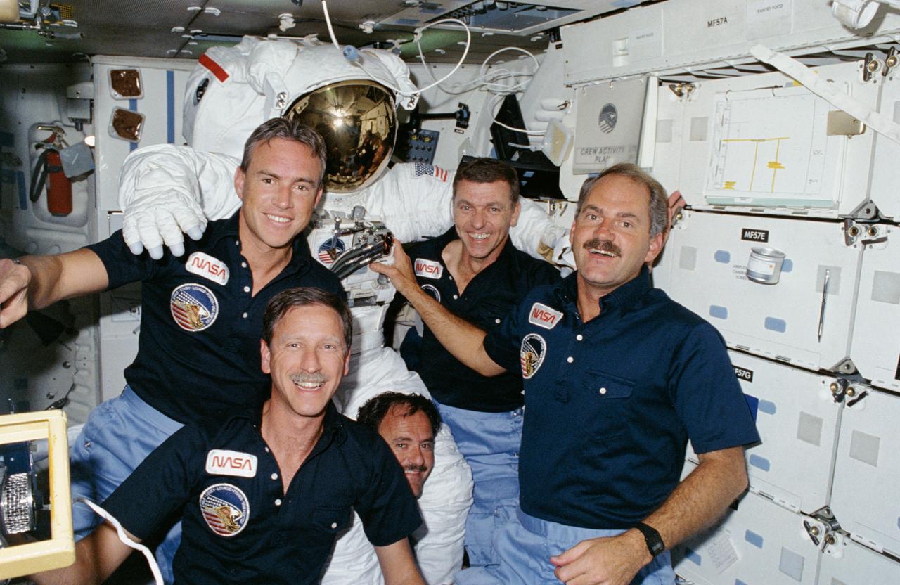 51I-07-015 (4-5 Sept 1985) --- All five STS 51-I crewmembers pose with one of two extravehicular mobility unit (EMU) spacesuits used by Astronauts van Hoften and Fisher on their two-day EVA.