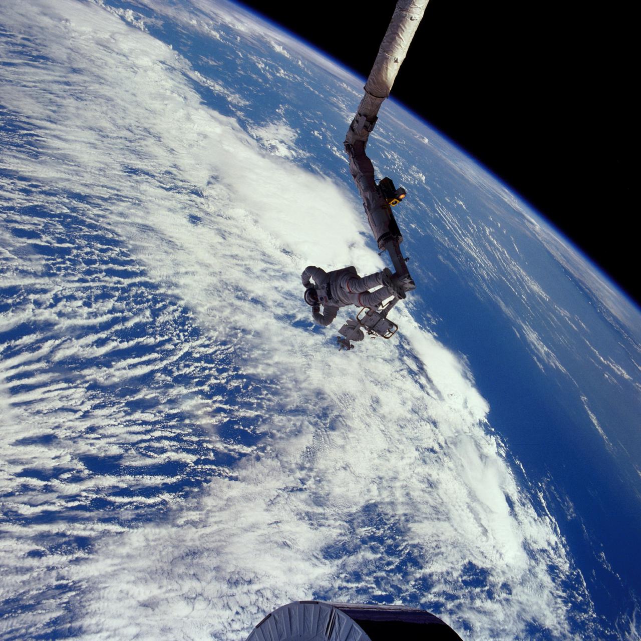 51I-41-086 (1 September 1985) --- Astronaut James D. van Hoften, mission specialist, flexes his muscles in celebration of a triumphant extravehicular task.  Clouds over the ocean form the backdrop for this 70mm scene, toward the end of a two-day effort to capture, repair and release the previously errant Syncom IV-3 communications satellite.  Van Hoften, anchored to a special foot restraint device on the end of Discovery's Remote Manipulator System (RMS), had just performed the final "shove" that started the relative separation of the Shuttle and the Syncom, which is not far out of frame.  He had been joined by astronaut William F. Fisher for the busy two days of EVA.