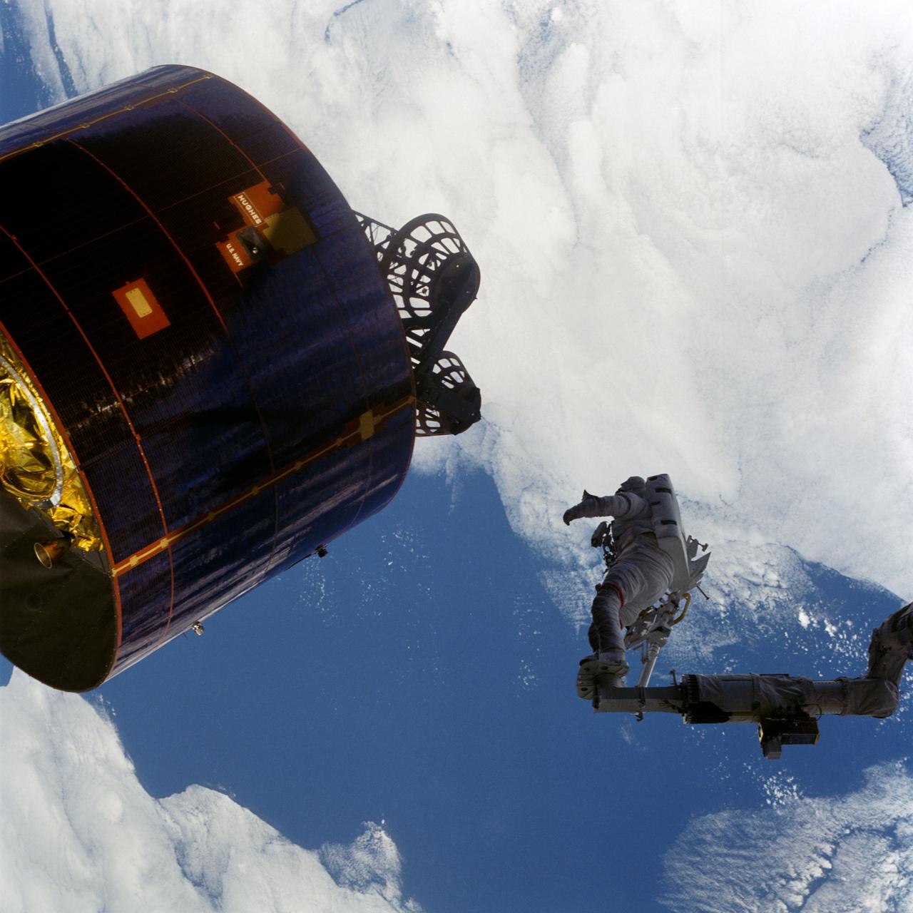 51I-44-012 (1 Sept. 1985) --- Astronaut James D. van Hoften looks on as the Syncom IVC-3 satellite responds to his push against it moments earlier.  Dr. van Hoften, mission specialist, is anchored to a foot restraint on the end of the remote manipulator system (RMS) arm of the Earth-orbiting space shuttle Discovery. The 51-I crew members showed this photograph at their Sept. 11 postflight press conference. Photo credit: NASA