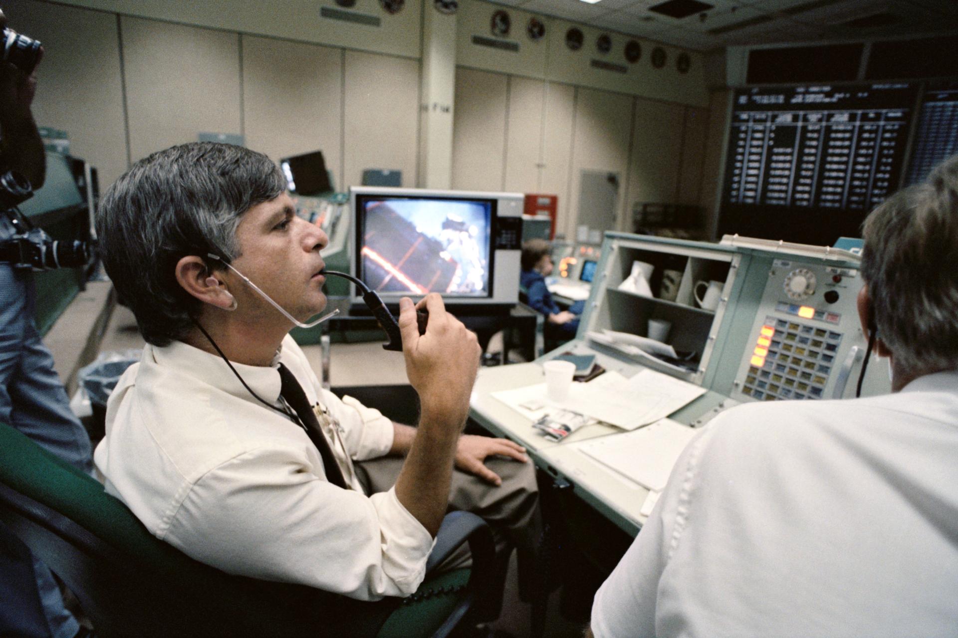 A flight controller smokes a pipe as he monitors the console at the mission control center.