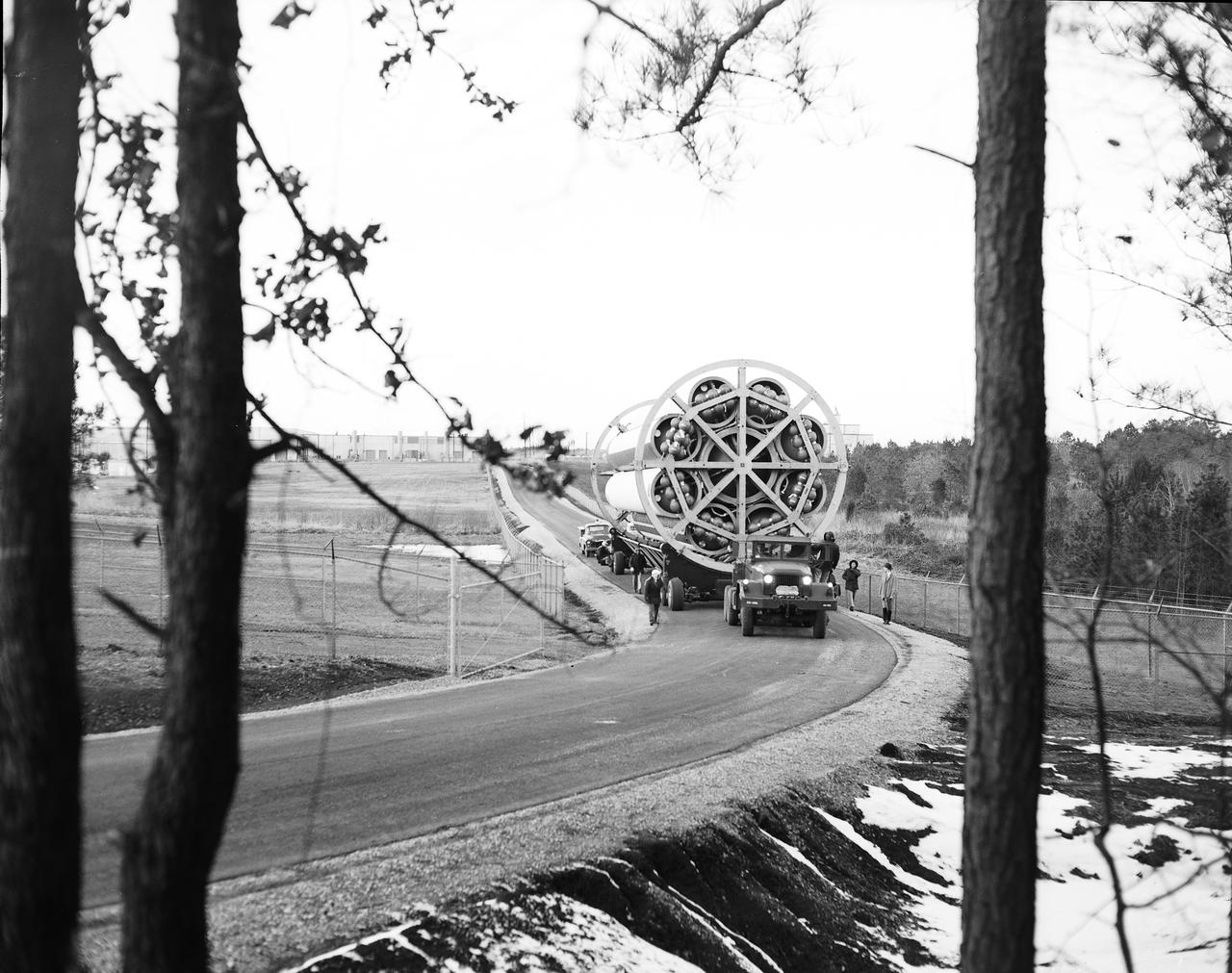 This photograph shows the Saturn-I first stage (S-1 stage) being transported to the test stand for a static test firing at the Marshall Space Flight Center. Soon after NASA began operations in October 1958, it was evident that sending people and substantial equipment beyond the Earth's gravitational field would require launch vehicles with weight-lifting capabilities far beyond any developed to that time. In early 1959, NASA accepted the proposal of Dr. Wernher von Braun for a multistage rocket, with a number of engines clustered in one or more of the stages to provide a large total thrust. The initiation of the Saturn launch vehicle program ultimately led to the study and preliminary plarning of many different configurations and resulted in production of three Saturn launch vehicles, the Saturn-I, Saturn I-B, and Saturn V. The Saturn family of launch vehicles began with the Saturn-I, a two-stage vehicle originally designated C-1. The research and development program was planned in two phases, or blocks: one for first stage development (Block I) and the second for both first and second stage development (Block-II). Saturn I had a low-earth-orbit payload capability of approximately 25,000 pounds. The design of the first stage (S-1 stage) used a cluster of propellant tanks containing liquid oxygen (LOX) and kerosene (RP-1), and eight H-1 engines, yielding a total thrust of 1,500,000 pounds. Of the ten Saturn-Is planned, the first eight were designed and built at the Marshall Space Flight Center, and the remaining two were built by the Chrysler Corporation.