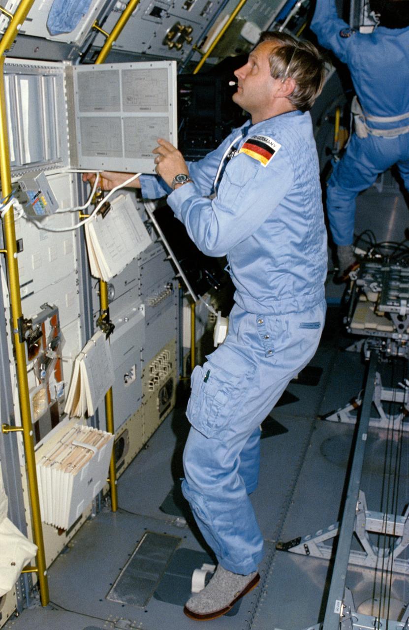 61A-01-032 (30 Oct-6 Nov 1985) --- West German Payload Specialist Ernst Messerschmid, foreground, opens a door on the materials science double rack (MSDR) to begin an experiment while Dutch Payload Specialist Wubbo J. Ockels performs a "run" on the vestibular sled in the background.