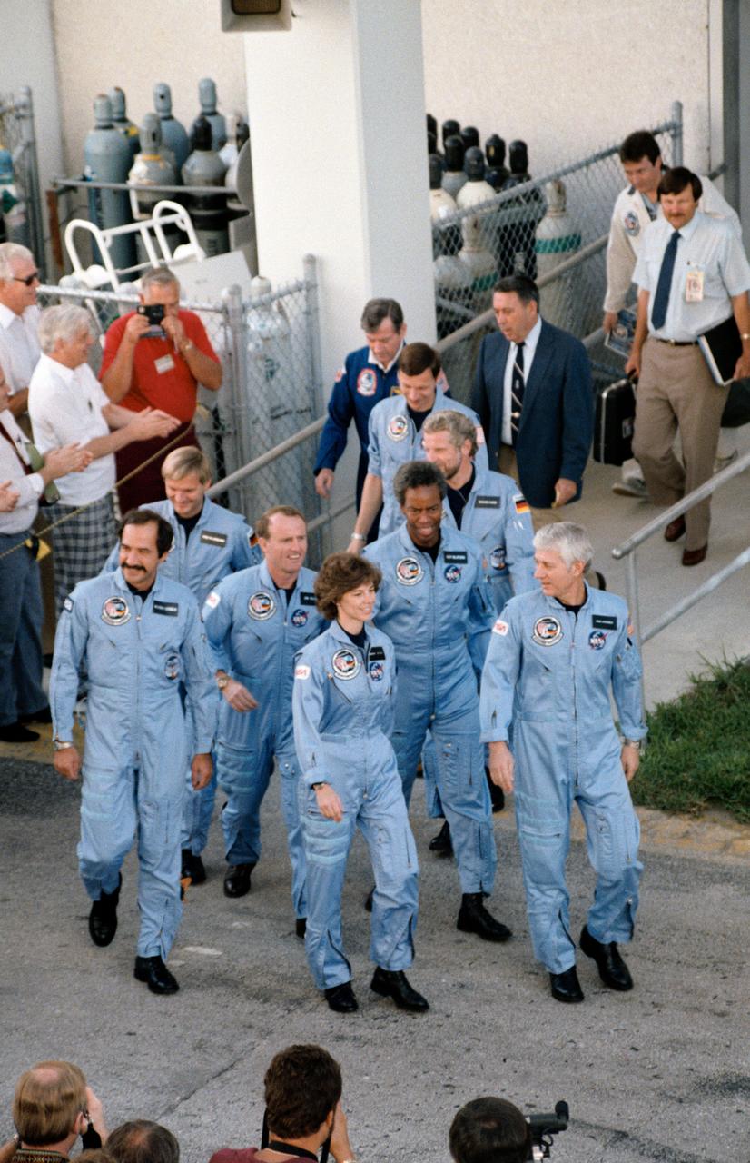 61A-S-015 (30 Oct 1985) --- A record number of crewmembers to serve on a Shuttle mission walks from the operations and checkout facility to a crew transfer van en route to Launch Pad 39A where the Challenger awaits the 61-A/Spacelab D-1launch.  Leading the way is Henry W. Hartsfield Jr., mission commander, as Steven R. Nagel, pilot, trails the blue-suited team members.  At center are James F. Buchli, Bonnie J. Dunbar and Guion S. Bluford Jr.--all mission specialists.  They are flanked by Wubbo J. Ockels and Ernst Messerschmid on the left and Reinhard Furrer on the right. John W. Young, chief of the astronaut office at JSC and George W.S. Abbey, director of flight crew operations at JSC, follow the crew.  Richard W. Nygren, assistant to the director, is in background.  Messerschmid and Furrer are German scientists and Ockels is a Dutch scientist; and the three will be working with NASA's three mission specialists in the D-1 science module during the week-long flight.