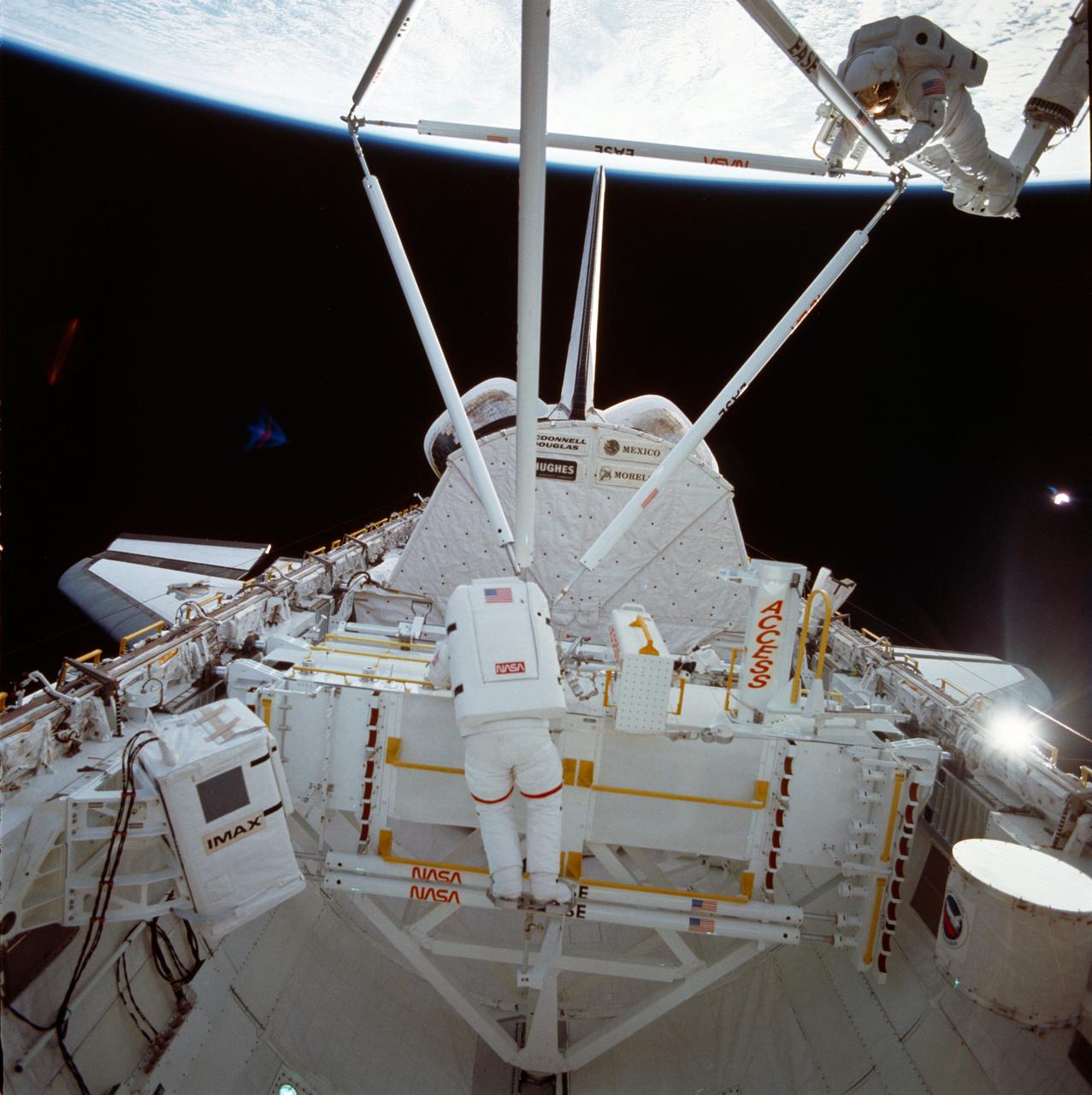 61B-41-047 (1 Dec 1985) --- Astronauts Jerry L. Ross (left) and Sherwood C. (Woody) Spring are photographed by Astronaut Bryan D. O'Connor as they continue to assemble more pieces of the EASE (Experimental Assembly of Structures in Extravehicular Activities) device during the week-long STS 61-B mission.  This frame is one of a series covering the structure's build-up.