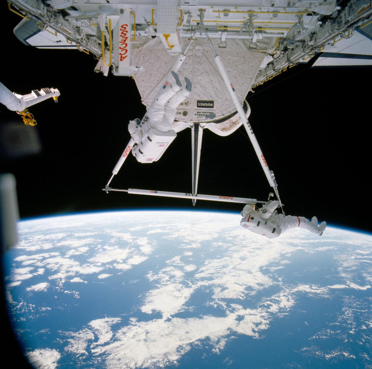 Astronauts Jerry L. Ross (left) and Sherwood C. (Woody) Spring are photographed as they assemble pieces of the Experimental Assembly of Structures in Extravehicular Activities (EASE) device in the open payload bay. The Canadian-built remote manipulator system (RMS) arm (partially obscured in the right portion of the frame) is in position to allow television cameras to record the activity.