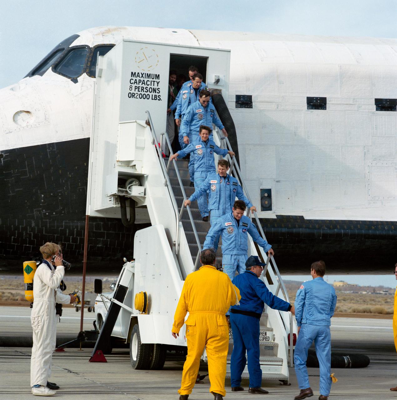 61B-S-071 (3 Dec 1985) --- George W.S. Abbey, director of flight crew operations at the Johnson Space Center (JSC), shakes hands with astronaut Brewster Shaw Jr., STS 61-B mission commander, as the seven-member crew descends the steps from its space-bound "home" for the last week. Following Shaw down the steps (bottom to top) were astronauts Bryan D. O'Connor, Sherwood C. Spring, Mary L. Cleave, Jerry L. Ross and Payload Specialists Charles D. Walker and Rodolfo Neri.