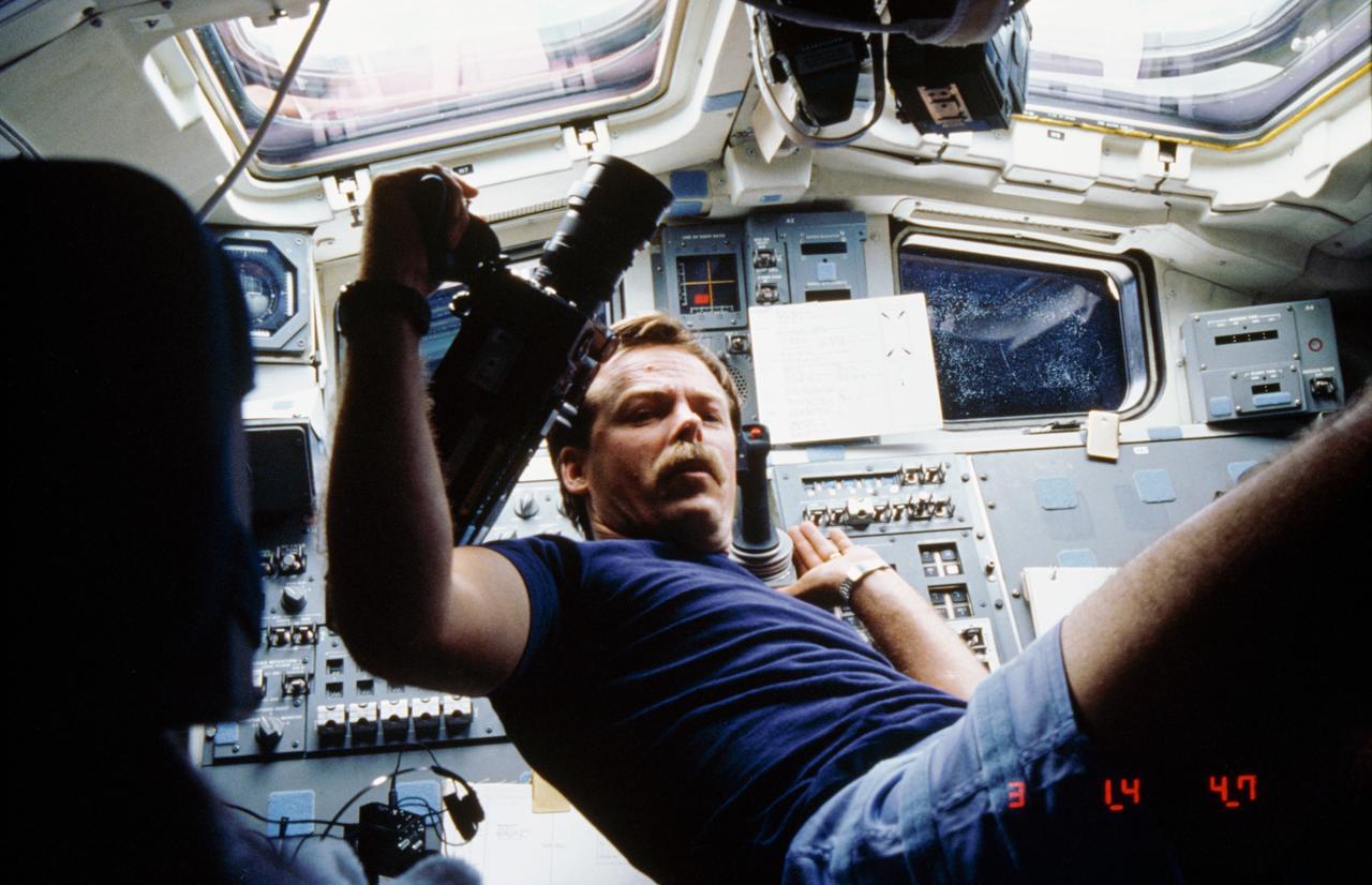 61C-07-030 (15 Jan 1986) --- Astronaut Robert L. Gibson, STS 61-C mission commander, partially floats on the aft flight deck of the earth-orbiting Space Shuttle Columbia while preparing to use a motion picture camera.  The windows overlooking the cargo bay are visible in the background.