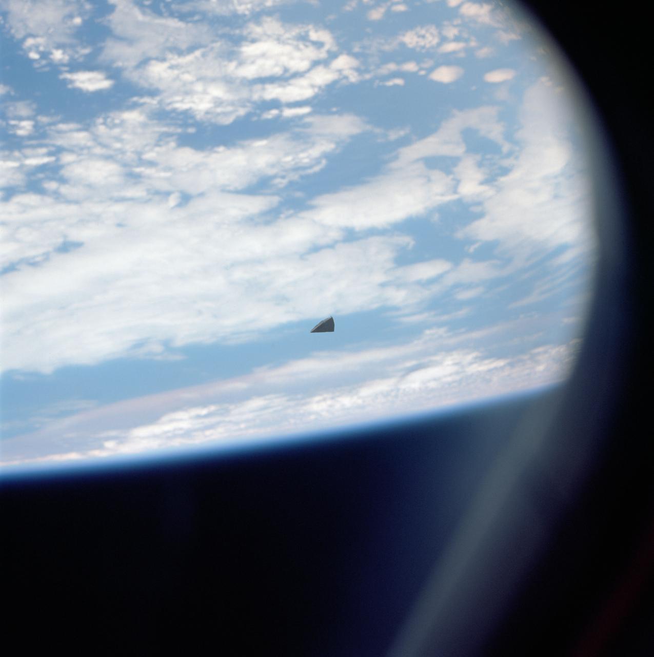 A small piece of thermal insulation tile floats in space near the Shuttle Columbia. The cloudy surface of the earth is used as a background.