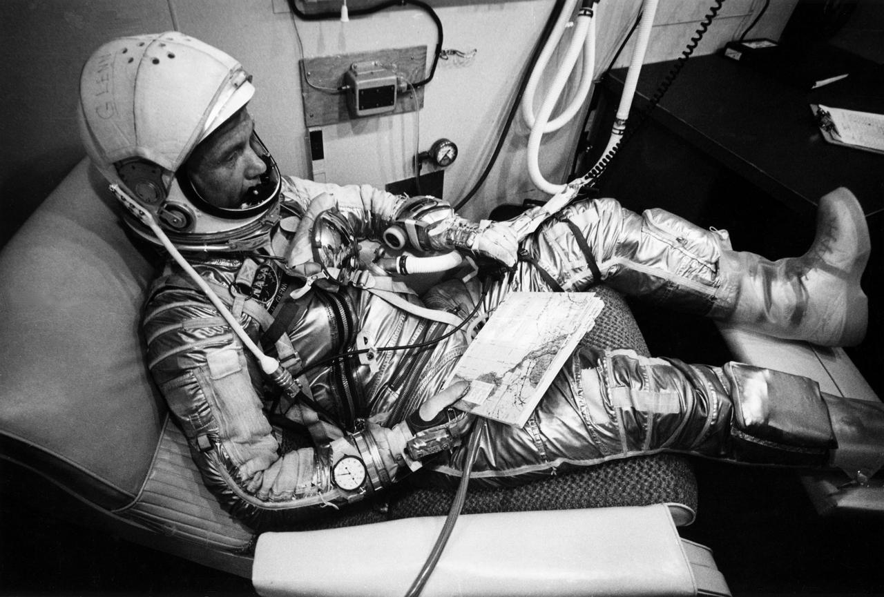 CAPE CANAVERAL, Fla. – John Glenn in flight suit prior to MA-6 launch at Cape Canaveral, Fla. He is relaxing on his contour couch in Hangar S early Feb. 20, 1962. Glanced over his flight maps in a last-minute check before leaving for his Friendship 7 space capsule and an orbital flight of the Earth. Glenn completed three orbits of the Earth and plunged to a safe landing in the Atlantic nearly five hours after blastoff.  Photo credit: NASA