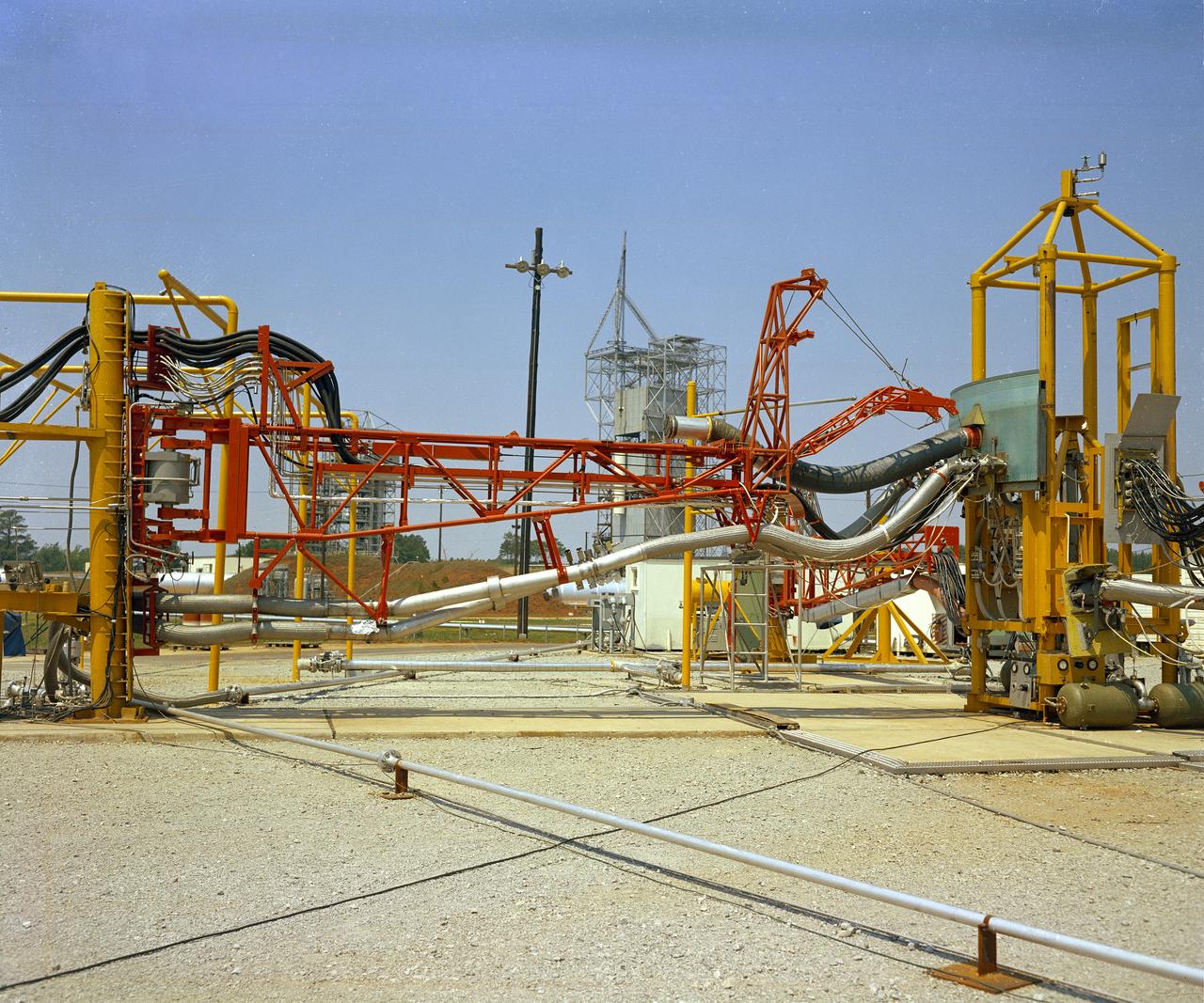 The Marshall Space Flight Center (MSFC) played a crucial role in the development of the huge Saturn rockets that delivered humans to the moon in the 1960s.  Many unique facilities existed at MSFC for the development and testing of the Saturn rockets.  Affectionately nicknamed “The Arm Farm”, the Random Motion/ Lift-Off Simulator was one of those unique facilities. This facility was developed to test the swingarm mechanisms that were used to hold the rocket in position until lift-off. The Arm Farm provided the capability of testing the detachment and reconnection of various arms under brutally realistic conditions.  The 18-acre facility consisted of more than a half dozen arm test positions and one position for testing access arms used by the Apollo astronauts. Each test position had two elements: a vehicle simulator for duplicating motions during countdown and launch; and a section duplicating the launch tower. The vehicle simulator duplicated the portion of the vehicle skin that contained the umbilical connections and personnel access hatches. Driven by a hydraulic servo system, the vehicle simulator produced relative motion between the vehicle and tower. On the Arm Farm, extreme environmental conditions (such as a launch scrub during an approaching Florida thunderstorm) could be simulated. The dramatic scenes that the Marshall engineers and technicians created at the Arm Farm permitted the gathering of crucial technical and engineering data to ensure a successful real time launch from the Kennedy Space Center. 