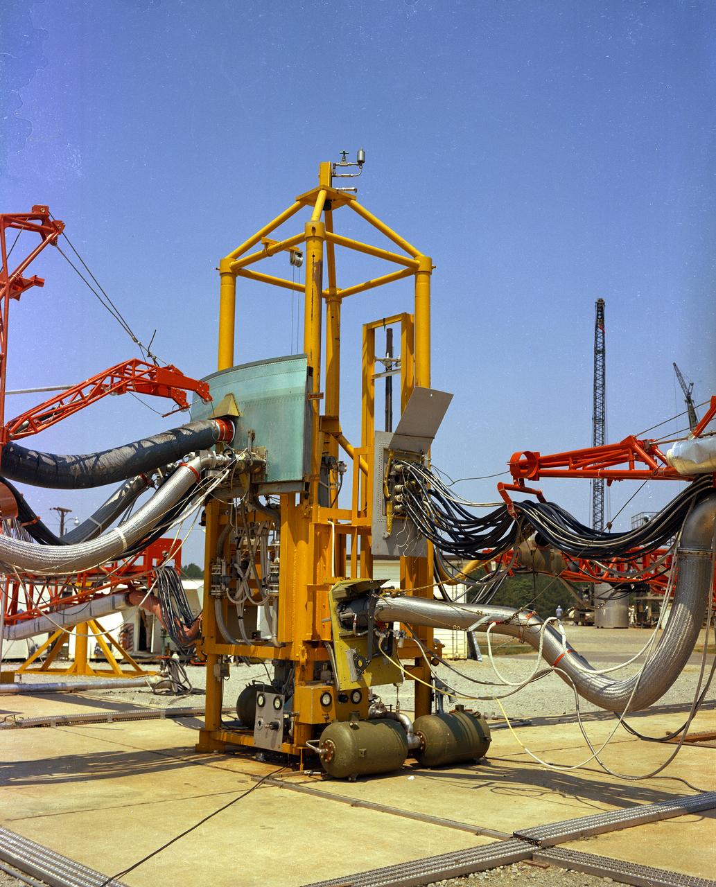 The Marshall Space Flight Center (MSFC) played a crucial role in the development of the huge Saturn rockets that delivered humans to the moon in the 1960s.  Many unique facilities existed at MSFC for the development and testing of the Saturn rockets.  Affectionately nicknamed “The Arm Farm”, the Random Motion/ Lift-Off Simulator was one of those unique facilities. This facility was developed to test the swingarm mechanisms that were used to hold the rocket in position until lift-off. The Arm Farm provided the capability of testing the detachment and reconnection of various arms under brutally realistic conditions.  The 18-acre facility consisted of more than a half dozen arm test positions and one position for testing access arms used by the Apollo astronauts. Each test position had two elements: a vehicle simulator for duplicating motions during countdown and launch; and a section duplicating the launch tower. The vehicle simulator duplicated the portion of the vehicle skin that contained the umbilical connections and personnel access hatches. Driven by a hydraulic servo system, the vehicle simulator produced relative motion between the vehicle and tower. On the Arm Farm, extreme environmental conditions (such as a launch scrub during an approaching Florida thunderstorm) could be simulated. The dramatic scenes that the Marshall engineers and technicians created at the Arm Farm permitted the gathering of crucial technical and engineering data to ensure a successful real time launch from the Kennedy Space Center. 