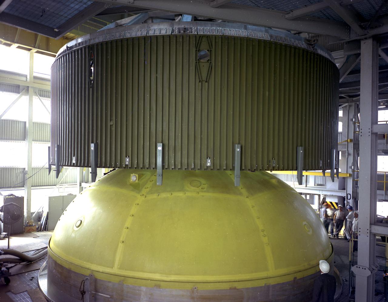 This photograph depicts a forward skirt being placed on the liquid oxygen tank for Saturn V S-IC (first) stage in the Manufacturing Engineering Laboratory at the Marshall Space Flight Center. Thirty-three feet in diameter, the fuel tanks hold a total of 4,400,000 pounds of fuel. Although this tankage was assembled at MSFC, the elements were made by the Boeing Company at Wichita and the Michoud Operations at New Orleans. 