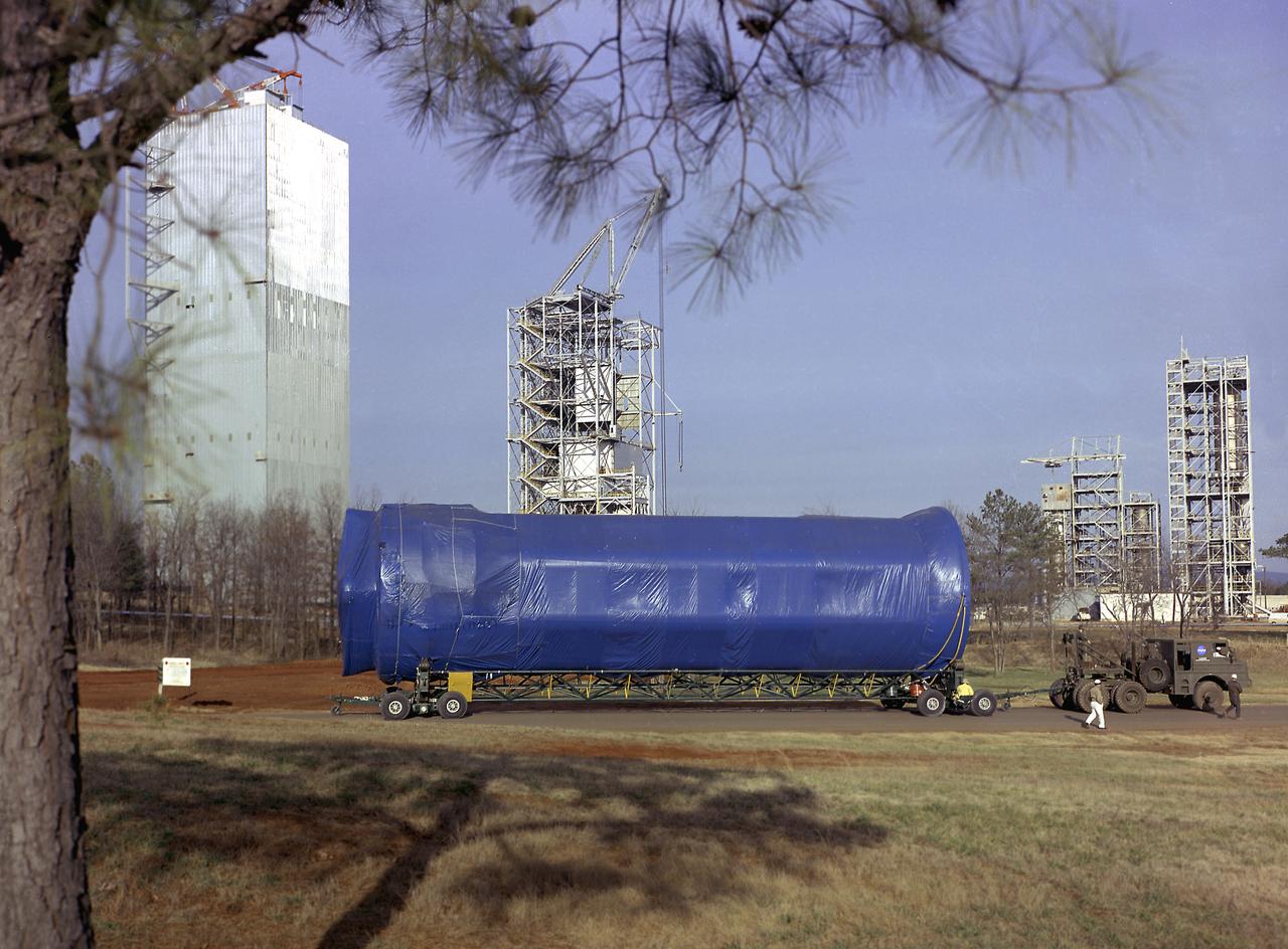 S-IB-200D, a dynamic test version of the Saturn IB launch vehicle's first stage (S-IB), makes its way to the Marshall Space Flight Center (MSFC) East Test Area on January 4, 1965. Test Laboratory persornel assembled a complete Saturn IB to test the structural soundness of the launch vehicle in the Dynamic Test Stand. Developed by the MSFC as an interim vehicle in MSFC's "building block" approach to the Saturn rocket development, the Saturn IB utilized Saturn I technology to further develop and refine the larger boosters and the Apollo spacecraft capabilities required for the manned lunar missions.