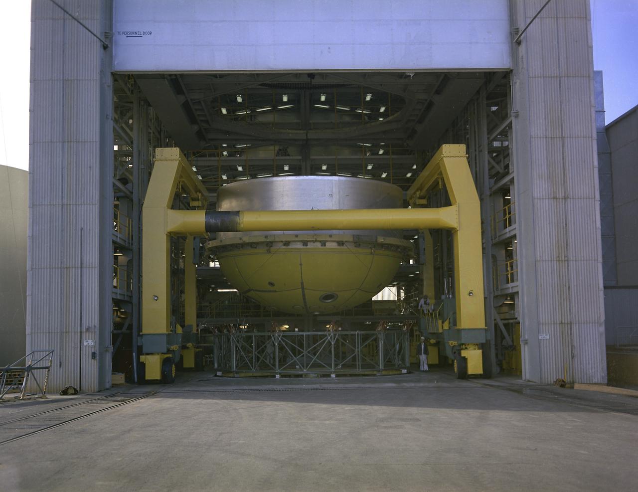 This photograph shows a fuel tank lower half for the Saturn V S-IC-T stage (the S-IC stage for static testing) on a C-frame transporter inside the vertical assembly building at the Marshall Space Flight Center.