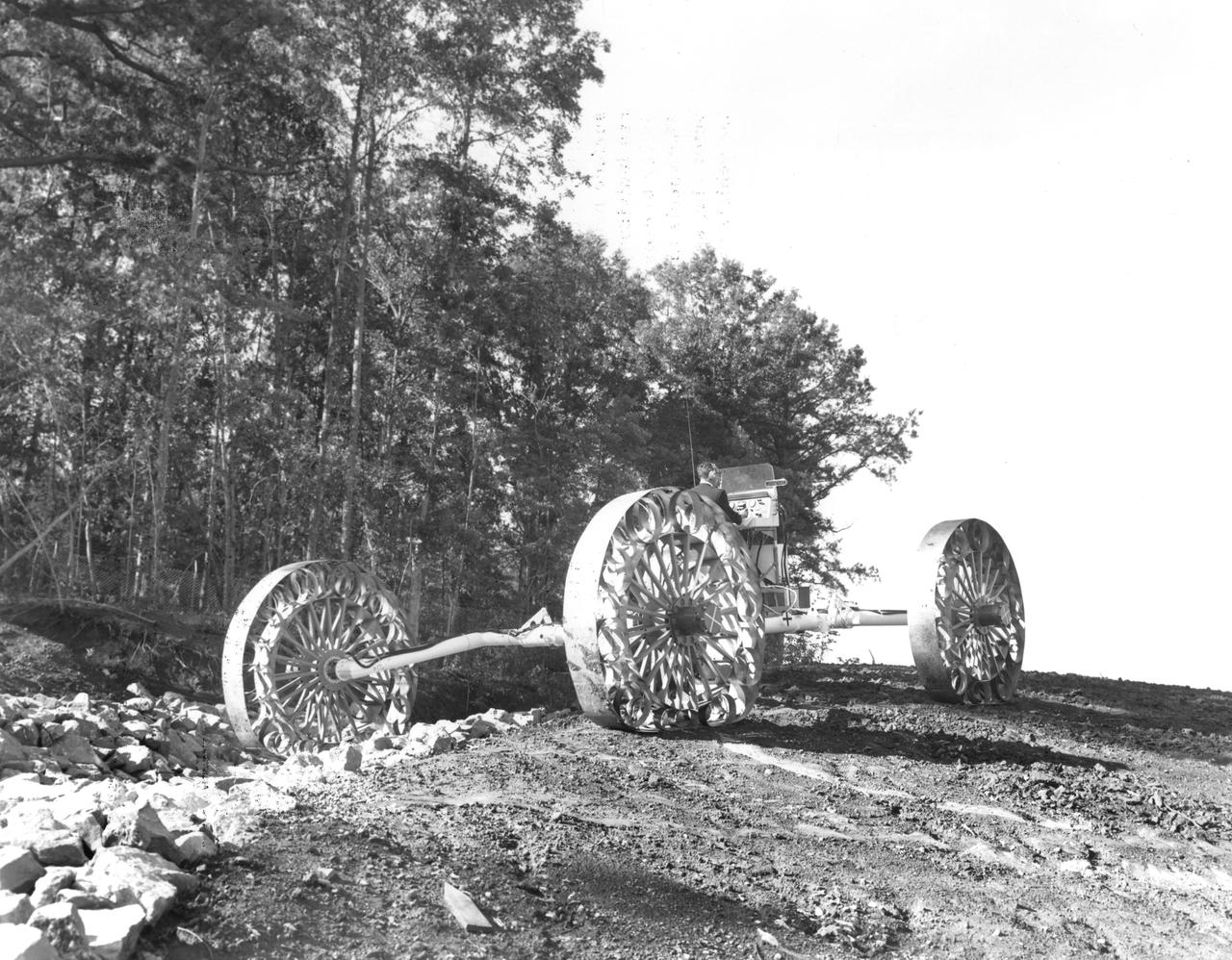 An engineer demonstrates a Mobility Test Article (MTA) at NASA’s Marshall Space Flight Center (MSFC). This unit, weighing 1/6th as much as an actual vehicle, was built by the Bendix Corporation and was one of the concepts of a possible Lunar Roving Vehicle (LRV). The data provided by the MTA helped in designing the Lunar Roving Vehicle (LRV), developed under the direction of MSFC. The LRV was designed to allow Apollo astronauts a greater range of mobility during lunar exploration missions. 