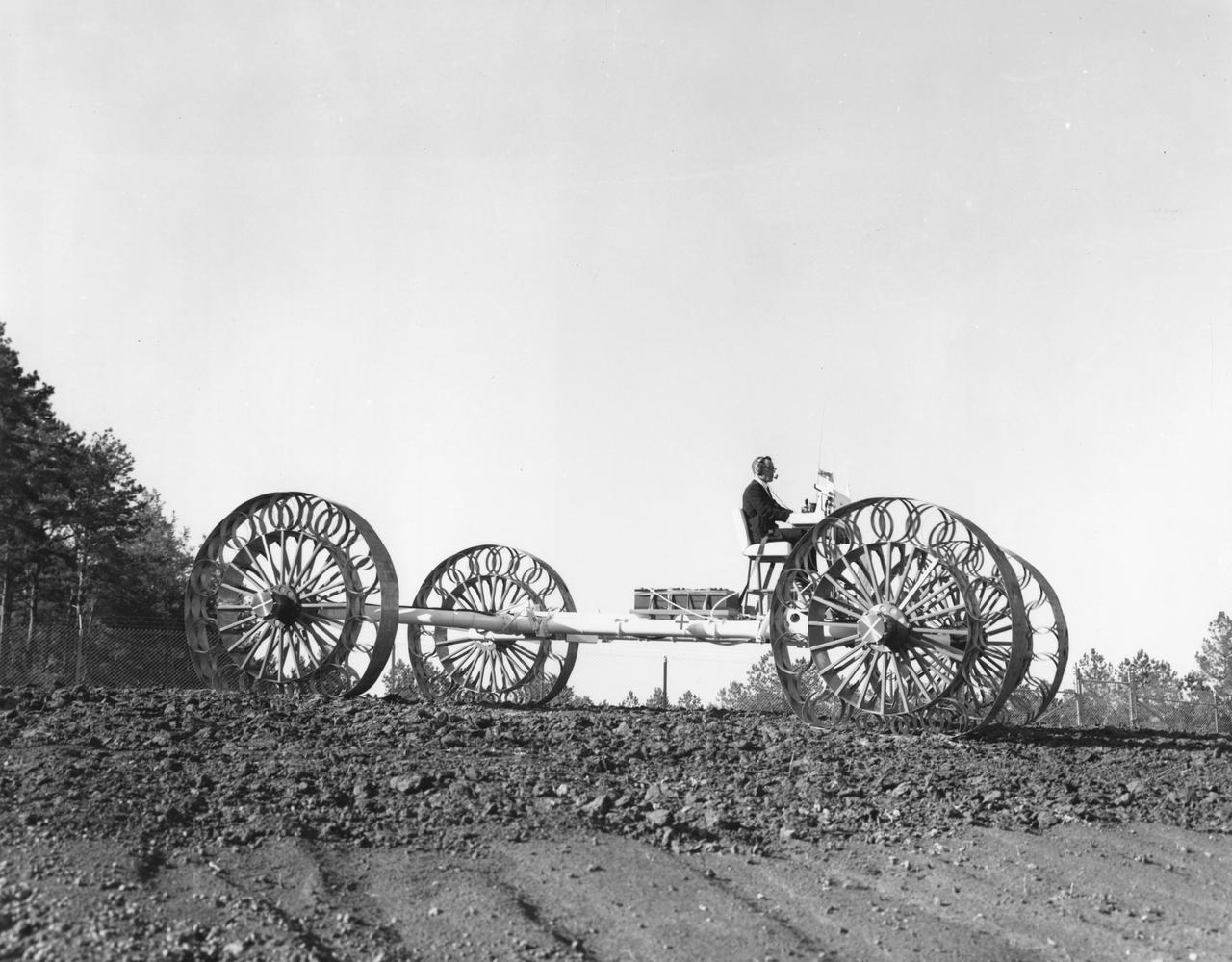 An engineer demonstrates a Mobility Test Article (MTA) at NASA’s Marshall Space Flight Center (MSFC). This unit, weighing 1/6th as much as an actual vehicle, was built by the Bendix Corporation and was one of the concepts of a possible Lunar Roving Vehicle (LRV). The data provided by the MTA helped in designing the Lunar Roving Vehicle (LRV), developed under the direction of MSFC. The LRV was designed to allow Apollo astronauts a greater range of mobility during lunar exploration missions. 