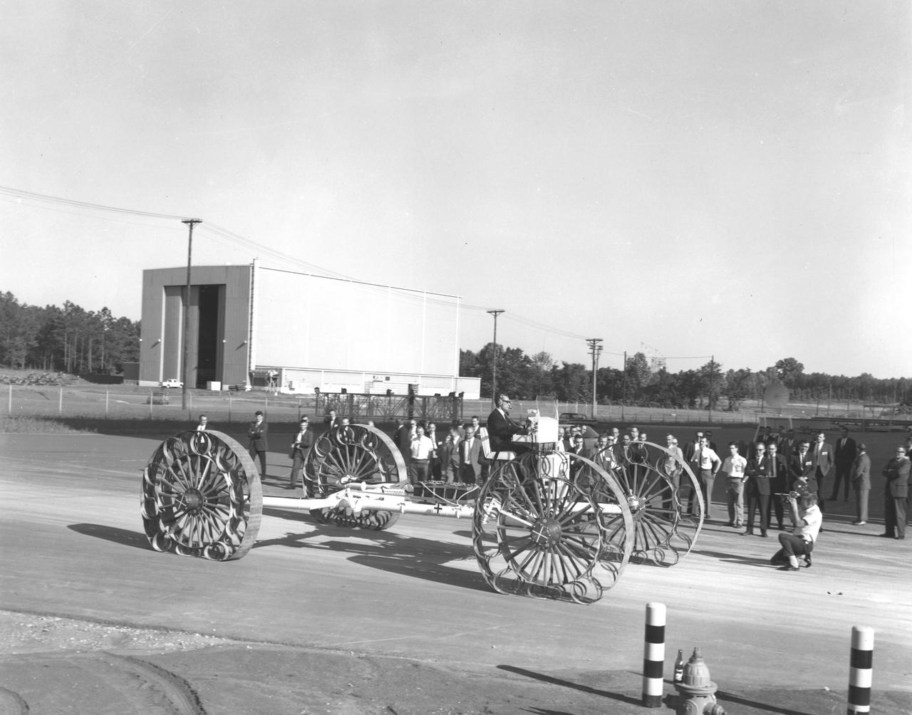 Newsmen watch a test engineer drive a Mobility Test Article (MTA) demonstrated at NASA’s Marshall Space Flight Center (MSFC). This unit, built by the Bendix Corporation, was one of the concepts of a possible Lunar Roving Vehicle (LRV). The data provided by the MTA helped in designing the LRV, developed under the direction of MSFC. The LRV was designed to allow Apollo astronauts a greater range of mobility during lunar exploration missions. 