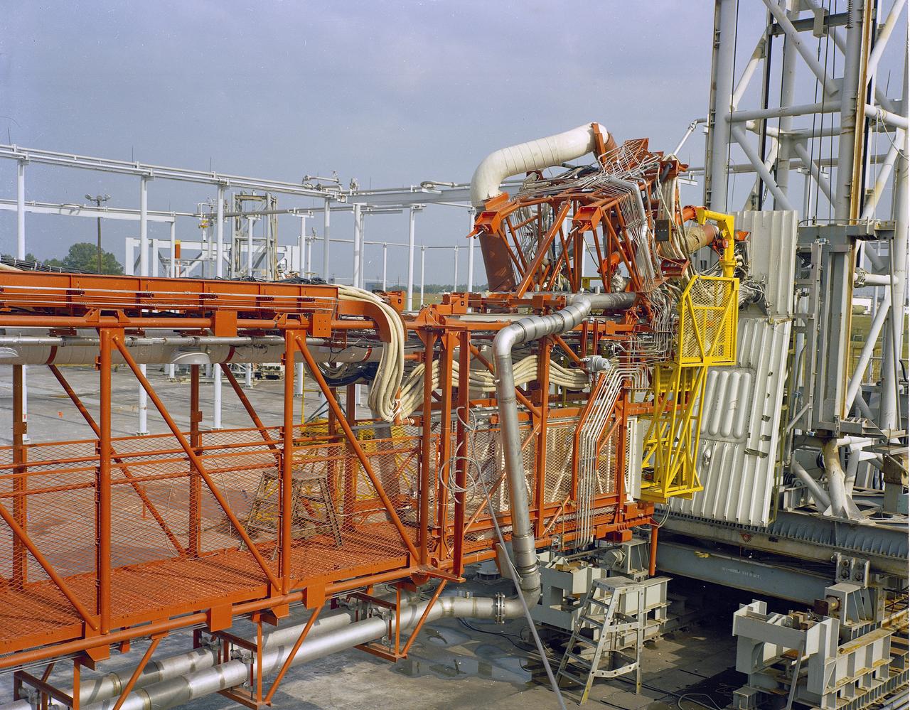 The Marshall Space Flight Center (MSFC) played a crucial role in the development of the huge Saturn rockets that delivered humans to the moon in the 1960s.  Many unique facilities existed at MSFC for the development and testing of the Saturn rockets.  Affectionately nicknamed “The Arm Farm”, the Random Motion/ Lift-Off Simulator was one of those unique facilities. This facility was developed to test the swingarm mechanisms that were used to hold the rocket in position until lift-off. The Arm Farm provided the capability of testing the detachment and reconnection of various arms under brutally realistic conditions.  The 18-acre facility consisted of more than a half dozen arm test positions and one position for testing access arms used by the Apollo astronauts. Each test position had two elements: a vehicle simulator for duplicating motions during countdown and launch; and a section duplicating the launch tower. The vehicle simulator duplicated the portion of the vehicle skin that contained the umbilical connections and personnel access hatches. Driven by a hydraulic servo system, the vehicle simulator produced relative motion between the vehicle and tower. On the Arm Farm, extreme environmental conditions (such as a launch scrub during an approaching Florida thunderstorm) could be simulated. The dramatic scenes that the Marshall engineers and technicians created at the Arm Farm permitted the gathering of crucial technical and engineering data to ensure a successful real time launch from the Kennedy Space Center. 