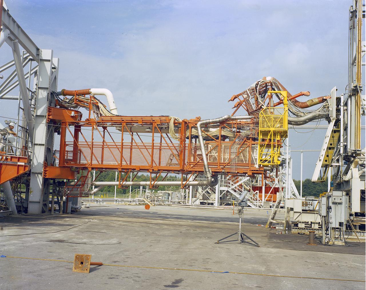 The Marshall Space Flight Center (MSFC) played a crucial role in the development of the huge Saturn rockets that delivered humans to the moon in the 1960s.  Many unique facilities existed at MSFC for the development and testing of the Saturn rockets.  Affectionately nicknamed “The Arm Farm”, the Random Motion/ Lift-Off Simulator was one of those unique facilities. This facility was developed to test the swingarm mechanisms that were used to hold the rocket in position until lift-off. The Arm Farm provided the capability of testing the detachment and reconnection of various arms under brutally realistic conditions.  The 18-acre facility consisted of more than a half dozen arm test positions and one position for testing access arms used by the Apollo astronauts. Each test position had two elements: a vehicle simulator for duplicating motions during countdown and launch; and a section duplicating the launch tower. The vehicle simulator duplicated the portion of the vehicle skin that contained the umbilical connections and personnel access hatches. Driven by a hydraulic servo system, the vehicle simulator produced relative motion between the vehicle and tower. On the Arm Farm, extreme environmental conditions (such as a launch scrub during an approaching Florida thunderstorm) could be simulated. The dramatic scenes that the Marshall engineers and technicians created at the Arm Farm permitted the gathering of crucial technical and engineering data to ensure a successful real time launch from the Kennedy Space Center. 