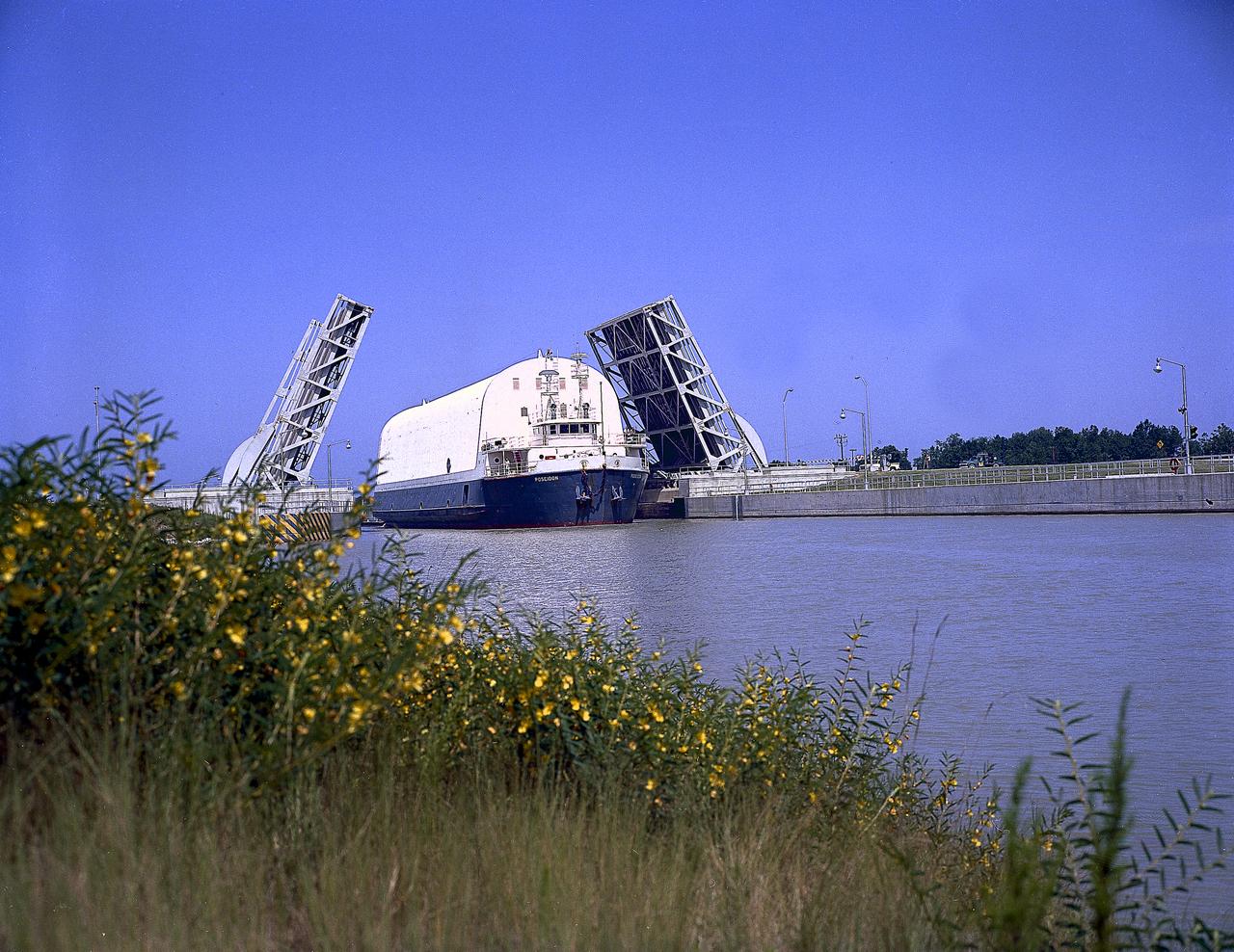 NASA used barges for transporting full-sized stages for the Saturn I, Saturn IB, and Saturn V vehicles between the Marshall Space Flight Center (MSFC), the manufacturing plant at the Michoud Assembly Facility (MAF), the Mississippi Test Facility for testing, and the Kennedy Space Center. The barges traveled from the MSFC dock to the MAF, a total of 1,086.7 miles up the Tennessee River and down the Mississippi River. The barges also transported the assembled stages of the Saturn vehicle from the MAF to the Kennedy Space Center, a total of 932.4 miles along the Gulf of Mexico and up along the Atlantic Ocean, for the final assembly and the launch. This photograph shows the barge Poseidon loaded with the Saturn V S-II (second) stage passing through a bascule bridge.