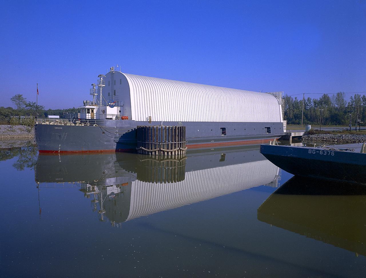 NASA used barges for transporting full-sized stages for the Saturn I, Saturn IB, and Saturn V vehicles between the Marshall Space Flight Center (MSFC), the manufacturing plant at the Michoud Assembly Facility (MAF), the Mississippi Test Facility for testing, and the Kennedy Space Center. The barges traveled from the MSFC dock to the MAF, a total of 1,086.7 miles up the Tennessee River and down the Mississippi River. The barges also transported the assembled stages of the Saturn vehicle from the MAF to the Kennedy Space Center, a total of 932.4 miles along the Gulf of Mexico and up along the Atlantic Ocean, for the final assembly and the launch. This photograph shows the barge Orion at the MSFC dock.