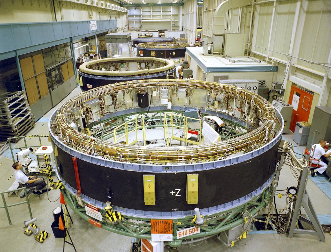 This is a view of the Saturn V instrument unit (IU) being manufactured in the east high bay at International Business Machines (IBM) in Huntsville, Alabama. IBM is a prime contractor for development and fabrication of the IU. The IU is vital to the proper flight of the vehicle. It contains navigation, guidance, control, and sequencing equipment for the launch vehicle. Three feet tall, twenty-one feet in diameter, and weighing about 4,000 pounds, the IU is mounted atop the S-IVB (third) stage, between the S-IVB stage and the Apollo spacecraft.