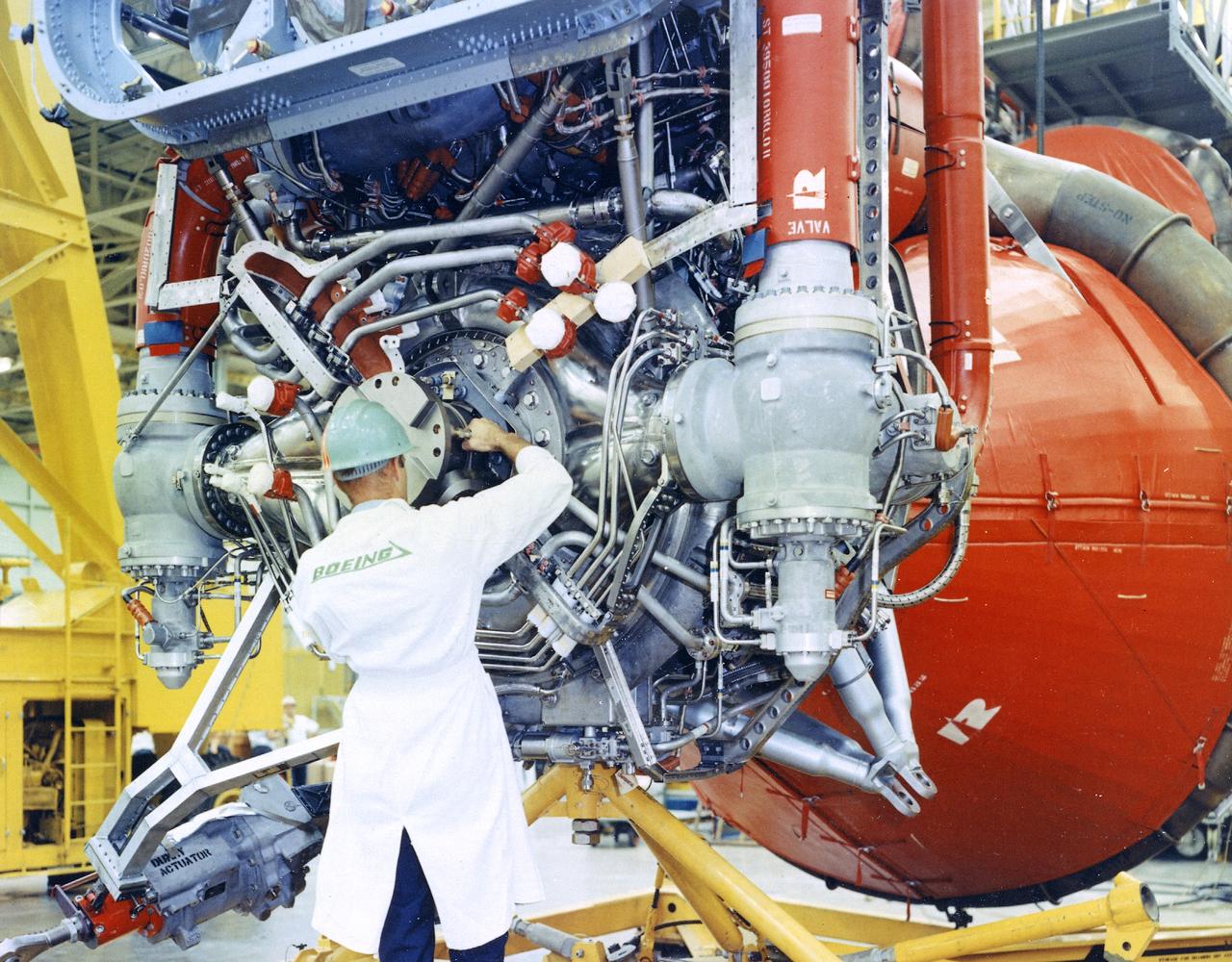 This image depicts a Boeing worker installing an F-1 engine on the Saturn V S-IC flight stage at the Michoud Assembly Facility (MAF). The Saturn IB and Saturn V first stages were manufactured at the MAF, located 24 kilometers (approximately 15 miles) east of downtown New Orleans, Louisiana. The prime contractors, Chrysler and Boeing, jointly occupied the MAF. The basic manufacturing building boasted 43 acres under one roof. By 1964, NASA added a separate engineering and office building, vertical assembly building, and test stage building. 