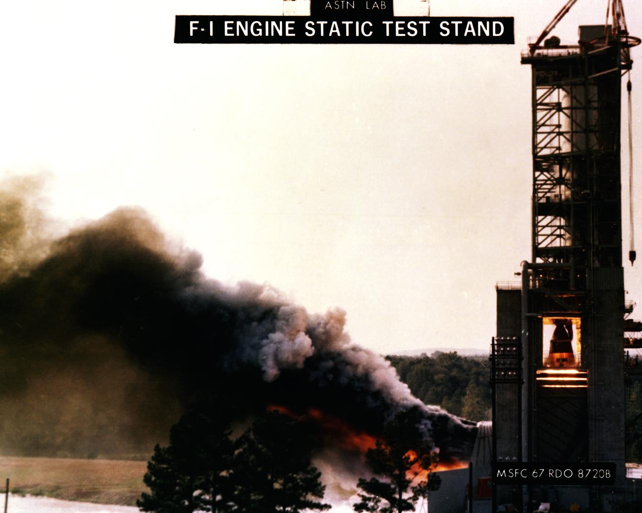 This photograph depicts the F-1 engine firing in the Marshall Space Flight Center’s F-1 Engine Static Test Stand. Construction of the S-IC Static test stand complex began in 1961 in the west test area of MSFC, and was completed in 1964. It is a vertical engine firing test stand, 239 feet in elevation and 4,600 square feet in area at the base, designed to assist in the development of the F-1 Engine. Capability is provided for static firing of 1.5 million pounds of thrust using liquid oxygen and kerosene. The foundation of the stand is keyed into the bedrock approximately 40 feet below grade.