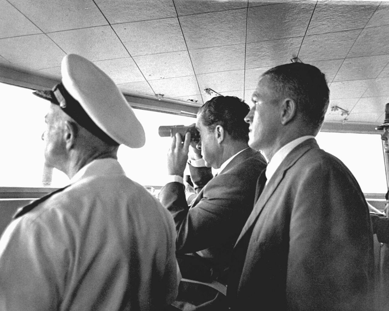 U.S. President Richard Milhous Nixon (center), aboard the U.S.S. Hornet aircraft carrier, used binoculars to watch the Apollo 11 Lunar Mission Recovery. Standing next to the President is astronaut Frank Borman, Apollo 8 Commander. The recovery operation took place in the Pacific Ocean where Navy para-rescue men recovered the capsule housing the 3-man Apollo 11 crew. The crew was airlifted to safety aboard the U.S.S. Hornet  where they were quartered in a Mobile Quarantine Facility (MQF) for 21 days post mission. The Apollo 11 mission, the first manned lunar mission, launched from the Kennedy Space Center, Florida via the Saturn V launch vehicle on July 16, 1969 and safely returned to Earth on July 24, 1969. The Saturn V vehicle was developed by the Marshall Space Flight Center (MSFC) under the direction of Dr. Wernher von Braun. Aboard were Neil A. Armstrong, commander; Michael Collins, Command Module (CM) pilot; and Edwin E. Aldrin Jr., Lunar Module (LM) pilot. The CM, piloted by Michael Collins remained in a parking orbit around the Moon while the LM, named “Eagle’’, carrying astronauts Neil Armstrong and Edwin Aldrin, landed on the Moon. Armstrong was the first human to ever stand on the lunar surface, followed by Edwin (Buzz) Aldrin.  During 2½ hours of surface exploration, the crew collected 47 pounds of lunar surface material for analysis back on Earth. With the success of Apollo 11, the national objective to land men on the Moon and return them safely to Earth had been accomplished. 
