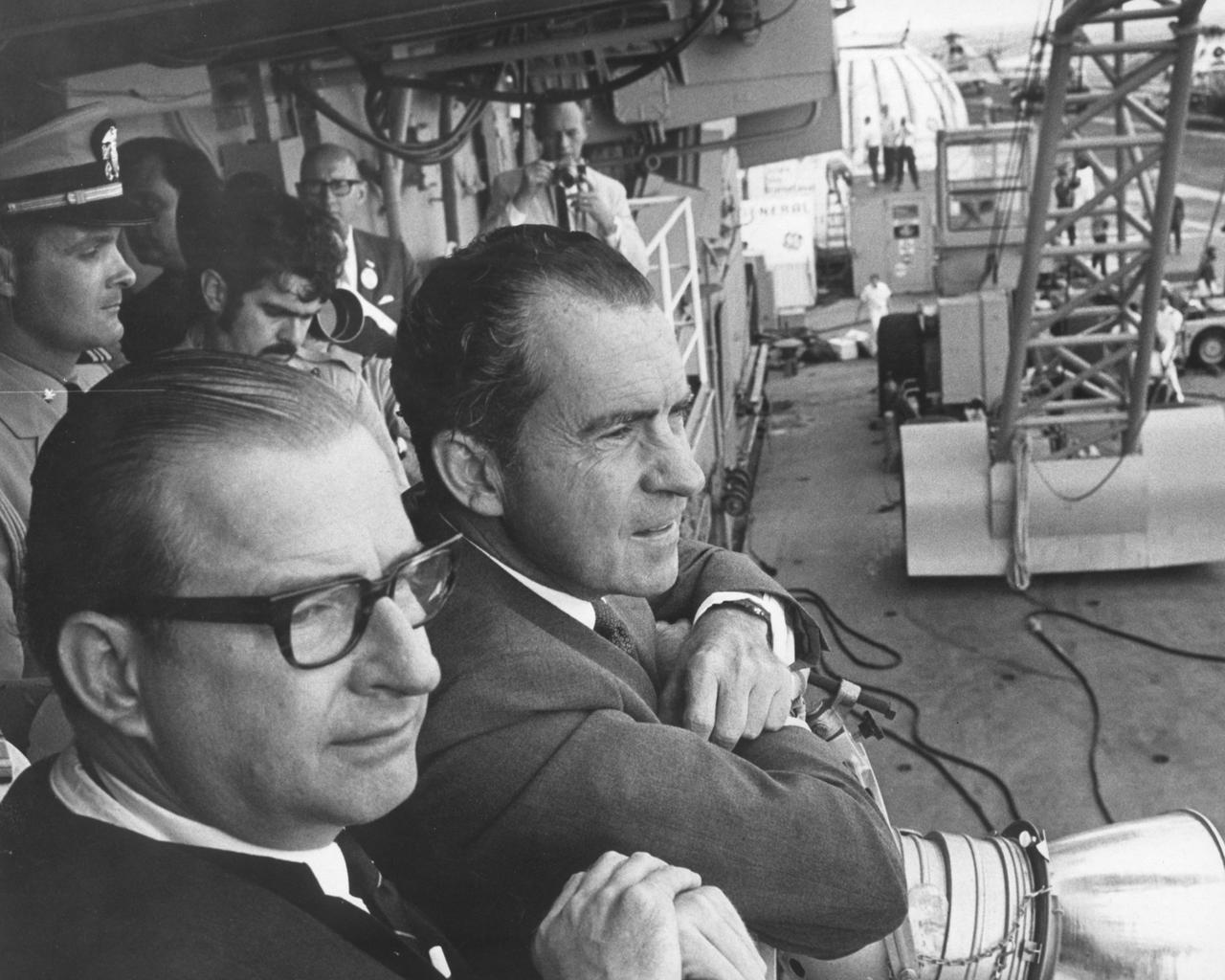 Dr. Thomas Paine, NASA administrator (left) and U.S. President Richard Milhous Nixon wait aboard the recovery ship, the U.S.S. Hornet, for splashdown of the Apollo 11 in the Pacific Ocean. Navy para-rescue men recovered the capsule housing the 3-man crew. The crew was taken to safety aboard the U.S.S. Hornet, where they were quartered in a Mobile Quarantine Facility (MQF). The Apollo 11 mission, the first manned lunar mission, launched from the Kennedy Space Center, Florida via the Saturn V launch vehicle on July 16, 1969 and safely returned to Earth on July 24, 1969. The Saturn V vehicle was developed by the Marshall Space Flight Center (MSFC) under the direction of Dr. Wernher von Braun. Aboard were Neil A. Armstrong, commander; Michael Collins, Command Module (CM) pilot; and Edwin E. Aldrin Jr., Lunar Module (LM) pilot. The CM, piloted by Michael Collins remained in a parking orbit around the Moon while the LM, named “Eagle’’, carrying astronauts Neil Armstrong and Edwin Aldrin, landed on the Moon. Armstrong was the first human to ever stand on the lunar surface, followed by Edwin (Buzz) Aldrin.  During 2½ hours of surface exploration, the crew collected 47 pounds of lunar surface material for analysis back on Earth. With the success of Apollo 11, the national objective to land men on the Moon and return them safely to Earth had been accomplished. 