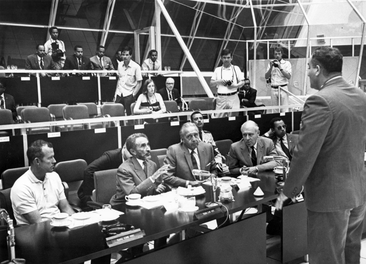 During a Kennedy Space Center (KSC) briefing on the next day’s Apollo 11 launch, Emperor Haile Selassie of Ethiopia (with raised hand) asks a question of Rocco A. Petrone, director of launch operations at KSC. To the right of the emperor is astronaut Gordon Cooper and to his left is Dr. Kurt Debus, director of KSC. The first manned lunar launch occurred at 9:32 am on July 16, 1969. The crew included astronauts Neil A. Armstrong, commander; Michael Collins, Command Module (CM) pilot; and Edwin E. Aldrin Jr., Lunar Module (LM) pilot. After 21/2 hours of collecting samples on the lunar surface, the crew safely splashed down into the Pacific Ocean on July 24, 1969. With the success of Apollo 11, the national objective to land men on the Moon and return them safely to Earth had been accomplished. 