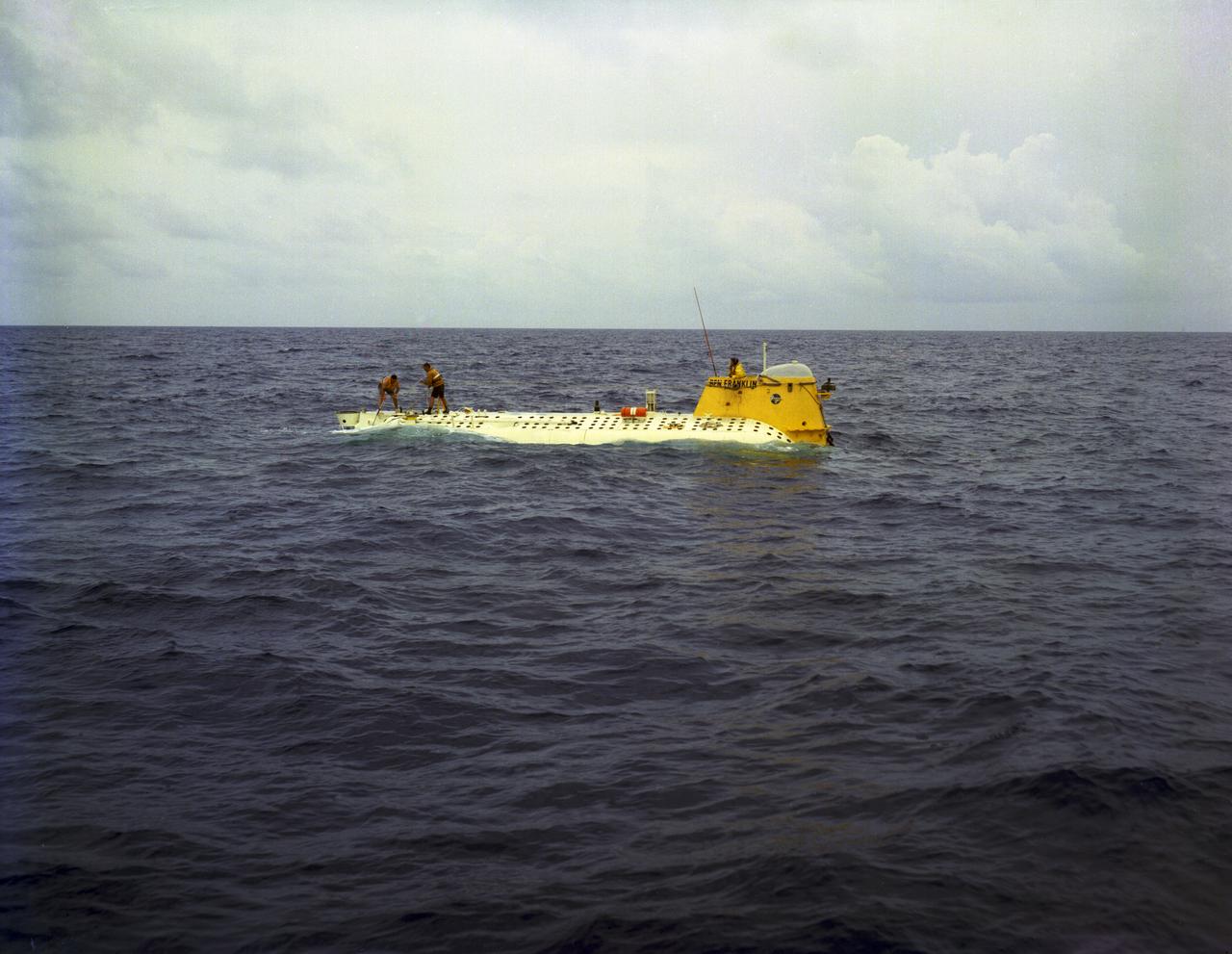 In this photograph, the deep-sea Research Submarine "Ben Franklin" drifts off the East Coast of the United States (U.S.) prior to submerging into the ocean. Named for American patriot and inventor Ben Franklin, who discovered the Gulf Steam, the 50-foot Ben Franklin was built between 1966 and 1968 in Switzerland for deep-ocean explorer Jacques Piccard and the Grumman Aircraft Engineering Corporation. The submersible made a famous 30-day drift dive off the East Coast of the United States and Canada in 1969 mapping the Gulf Stream's currents and sea life, and also made space exploration history by studying the behavior of aquanauts in a sealed, self-contained, self-sufficient capsule for NASA. On July 14, 1969, the Ben Franklin was towed to the high-velocity center of the Stream off the coast of Palm Beach, Florida. With a NASA observer on board, the sub descended to 1,000 feet off of Riviera Beach, Florida and drifted 1,400 miles north with the current for more than four weeks, reemerging near Maine. During the course of the dive, NASA conducted exhaustive analyses of virtually every aspect of onboard life. They measured sleep quality and patterns, sense of humor and behavioral shifts, physical reflexes, and the effects of a long-term routine on the crew. The submarine's record-shattering dive influenced the design of Apollo and Skylab missions and continued to guide NASA scientists as they devised future marned space-flight missions.