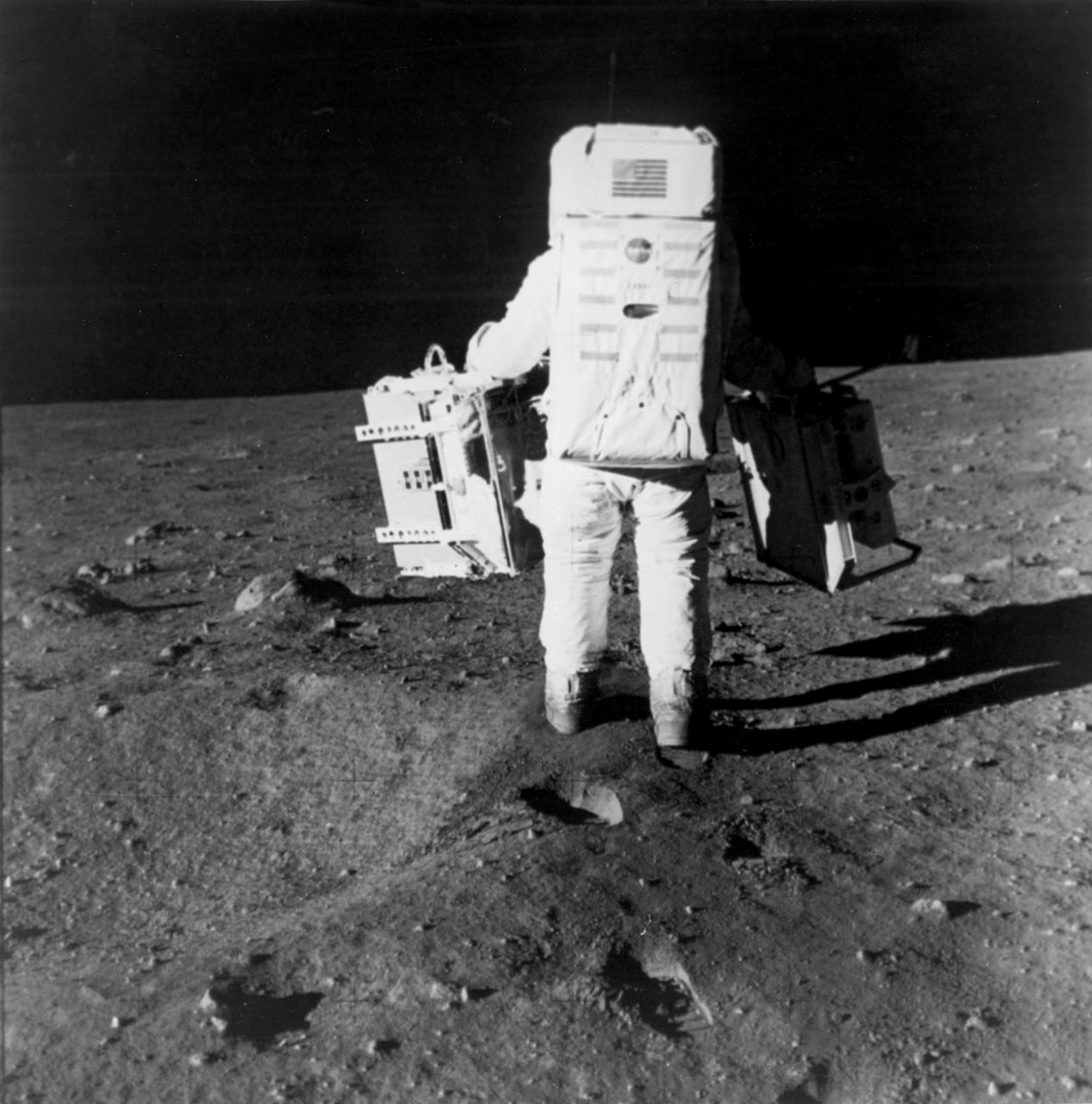 The first manned lunar landing mission, Apollo 11, launched from the Kennedy Space Center (KSC) in Florida via the Marshall Space Flight Center (MSFC) developed Saturn V launch vehicle on July 16, 1969 and safely returned to Earth on July 24, 1969. Aboard the space craft were astronauts Neil A. Armstrong, commander; Michael Collins, Command Module (CM) pilot; and Edwin E. (Buzz) Aldrin Jr., Lunar Module (LM) pilot. The CM, piloted by Michael Collins, remained in a parking orbit around the Moon, while the LM, named “Eagle’’, carrying astronauts Armstrong and Aldrin, landed on the Moon in the Sea of Tranquility. During 2½ hours of surface exploration, the crew set up experiments, collected 47 pounds of lunar surface material for analysis back on Earth, planted the U.S Flag, and left a message for all mankind. In this photograph, Aldrin walks past some rocks, easily carrying scientific equipment which would have been too heavy to carry on Earth. The two packages made up the Early Apollo Scientific Experiment Package (EASEP) on Apollo 11. On the left is the Passive Seismic Experiment Package (PSEP) and on the right is the Laser Ranging Retroreflector (LRR). 