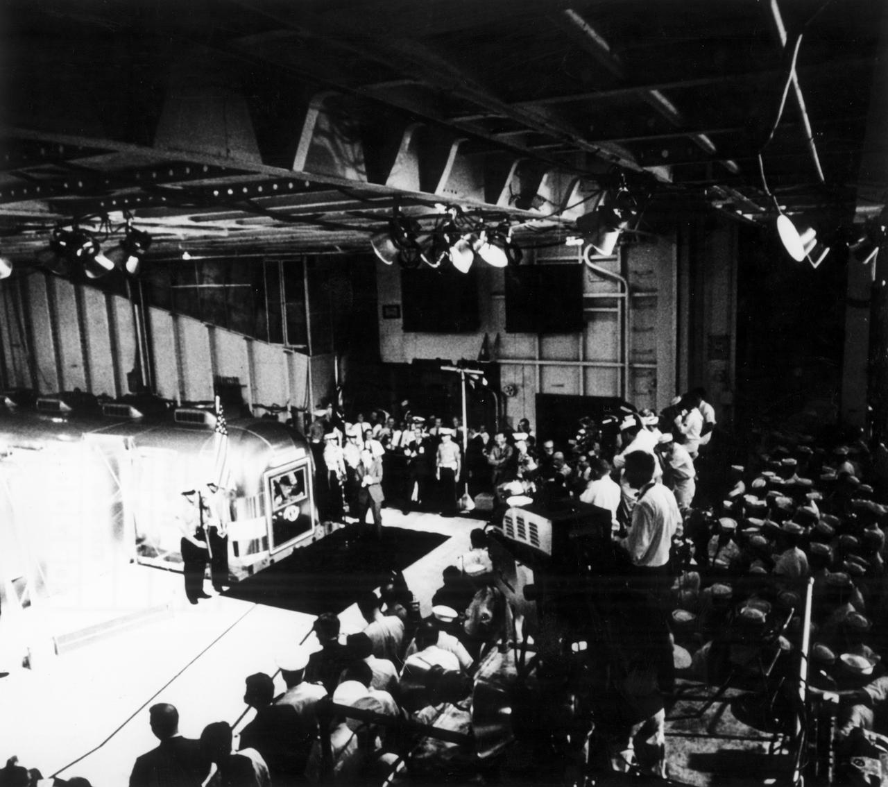 The Apollo 11 mission, the first manned lunar mission, launched from the Kennedy Space Center, Florida via the Marshall Space Flight Center (MSFC) developed Saturn V launch vehicle on July 16, 1969 and safely returned to Earth on July 24, 1969. Aboard the space craft were astronauts Neil A. Armstrong, commander; Michael Collins, Command Module (CM) pilot; and Edwin E. Aldrin Jr., Lunar Module (LM) pilot. The CM, piloted by Michael Collins remained in a parking orbit around the Moon while the LM, named “Eagle’’, carrying astronauts Neil Armstrong and Edwin Aldrin, landed on the Moon. During 2½ hours of surface exploration, the crew collected 47 pounds of lunar surface material for analysis back on Earth. The recovery operation took place in the Pacific Ocean where Navy para-rescue men recovered the capsule housing the 3-man Apollo 11 crew. The crew was airlifted to safety aboard the U.S.S. Hornet recovery ship, where they were quartered in a Mobile Quarantine Facility (MQF). In this photograph, the U.S.S. Hornet crew looks on as the quarantined Apollo 11 crew is addressed by U.S. President Richard Milhous Nixon via microphone and intercom. The president was aboard the recovery vessel awaiting return of the astronauts. With the success of Apollo 11, the national objective to land men on the Moon and return them safely to Earth had been accomplished.                                            