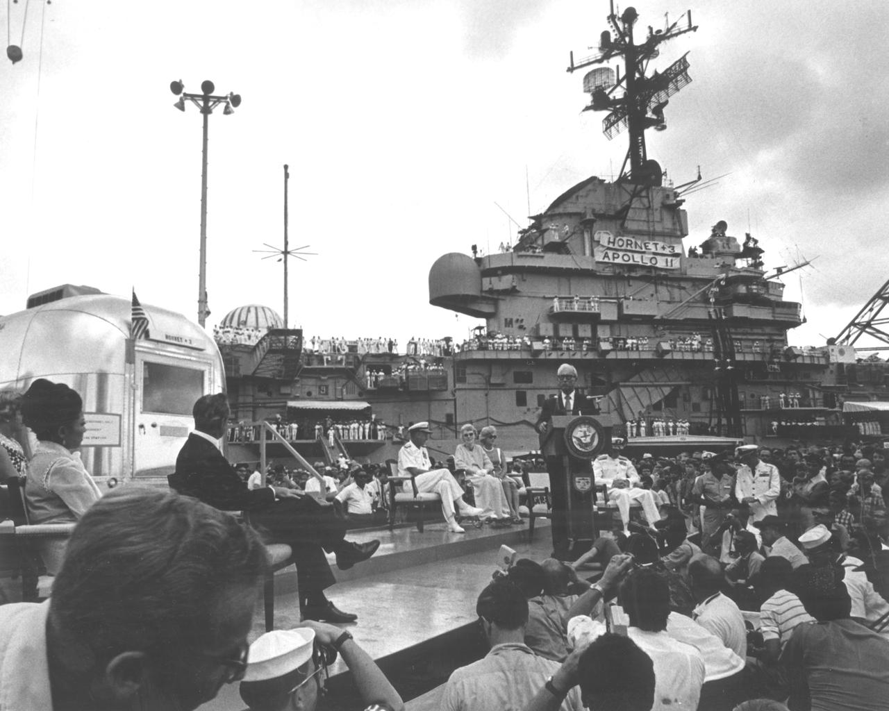 The Apollo 11 mission, the first manned lunar mission, launched from the Kennedy Space Center, Florida via the Marshall Space Flight Center (MSFC) developed Saturn V launch vehicle on July 16, 1969 and safely returned to Earth on July 24, 1969. Aboard the space craft were astronauts Neil A. Armstrong, commander; Michael Collins, Command Module (CM) pilot; and Edwin E. Aldrin Jr., Lunar Module (LM) pilot. The CM, piloted by Michael Collins remained in a parking orbit around the Moon while the LM, named “Eagle’’, carrying astronauts Neil Armstrong and Edwin Aldrin, landed on the Moon. During 2½ hours of surface exploration, the crew collected 47 pounds of lunar surface material for analysis back on Earth. The recovery operation took place in the Pacific Ocean where Navy para-rescue men recovered the capsule housing the 3-man Apollo 11 crew. The crew was airlifted to safety aboard the U.S.S. Hornet recovery ship, where they were quartered in a Mobile Quarantine Facility (MQF) for 21 days. The recovery vessel docked in Pearl Harbor Hawaii, where the occupied MQF was transferred for transport to the to NASA Manned Spacecraft Center (MSC) Lunar Receiving Laboratory in Houston, Texas. In this photo the quarantined astronauts are addressed by Hawaiian Governor John Burns upon their arrival at Pearl Harbor.