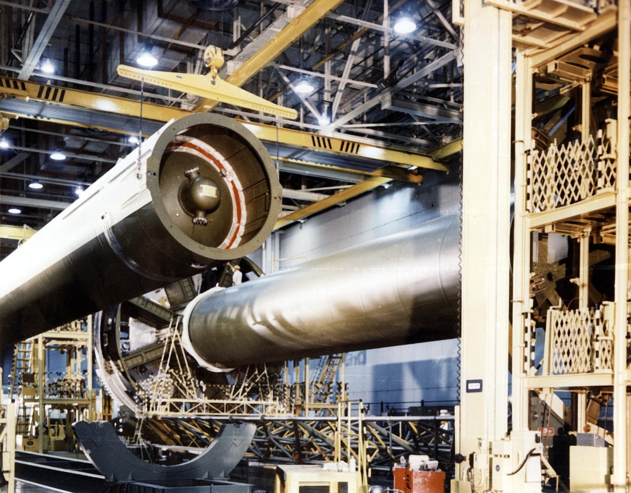 In the "clustering" procedure, an initial assembly step for the first stage (S-IB stage) of the Saturn IB launch vehicle, workers at the Michoud Assembly Facility (MAF) near New Orleans, Louisiana, place the first of eight outboard fuel tanks (left) next to the central liquid-oxygen tank of S-IB stage. Developed by the Marshall Space Flight Center (MSFC) and built by the Chrysler Corporation at MAF, the S-IB stage utilized eight H-1 engines to produce a combined thrust of 1,600,000 pounds. 