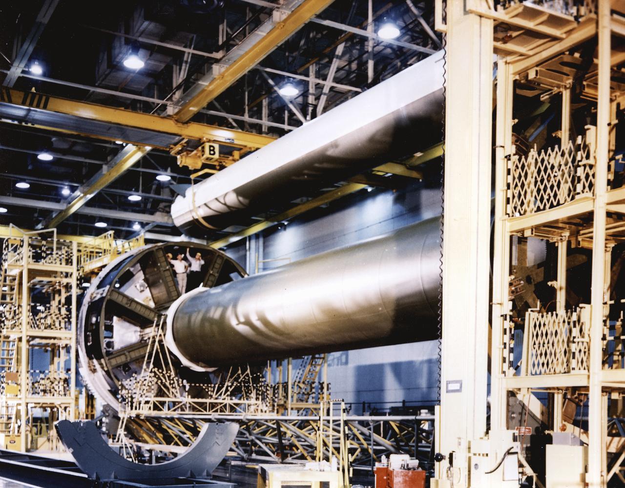 In the clustering procedure, an initial assembly step for the first stage (S-IB stage) of the Saturn IB launch vehicle, workers at the Michoud Assembly Facility (MAF) near New Orleans, Louisiana, place the first of eight outboard fuel tanks next to the central liquid-oxygen tank of the S-IB stage. Developed by the Marshall Space Flight Center (MSFC) and built by the Chrysler Corporation at MAF, the S-IB stage utilized eight H-1 engines to produce a combined thrust of 1,600,000 pounds. 