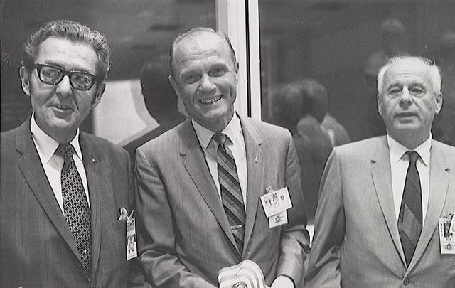 S69-44022 (7-24-69) --- On hand in Houston's mission control center to witness activity associated with the landing and recovery operations for the Apollo 11 mission were, from the left, Bob Kline, chief of the Mission Operations Procurement Branch at the Manned Spacecraft Center (MSC); astronaut John H. Glenn Jr.; and Eberhard Rees, deputy director of the Marshall Space Flight Center (MSFC). They were among a large number of personnel on hand in the MCC's mission operations control room (MOCR). Glenn holds one of the dozens of flags that were handed out for the return's celebration.