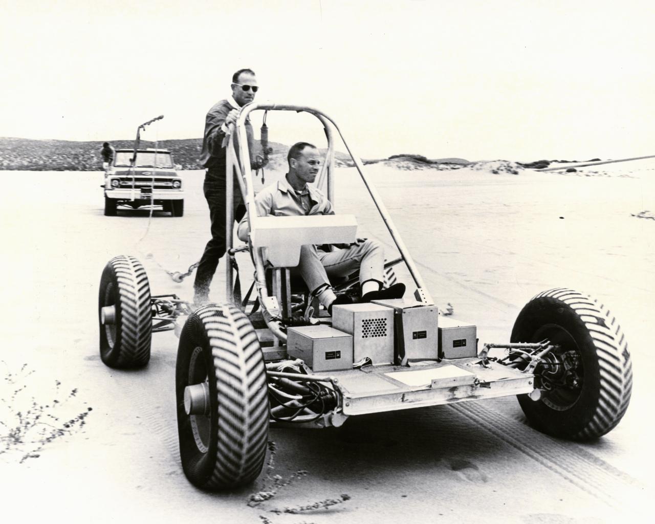 Astronauts Jack Lousma (seated) and Gerald Carr tested the Lunar Roving Vehicle (LRV) training unit on the sands near Pismo Beach.  The vehicle was built by the AC Delco electronics division of General Motors Corporation.  Under the direction of Marshall Space Flight Center (MSFC), the LRV was designed to allow Apollo astronauts a greater range of mobility during lunar exploration missions. The LRVs were deployed during the last three Apollo missions; Apollo 15, Apollo 16, and Apollo 17. 